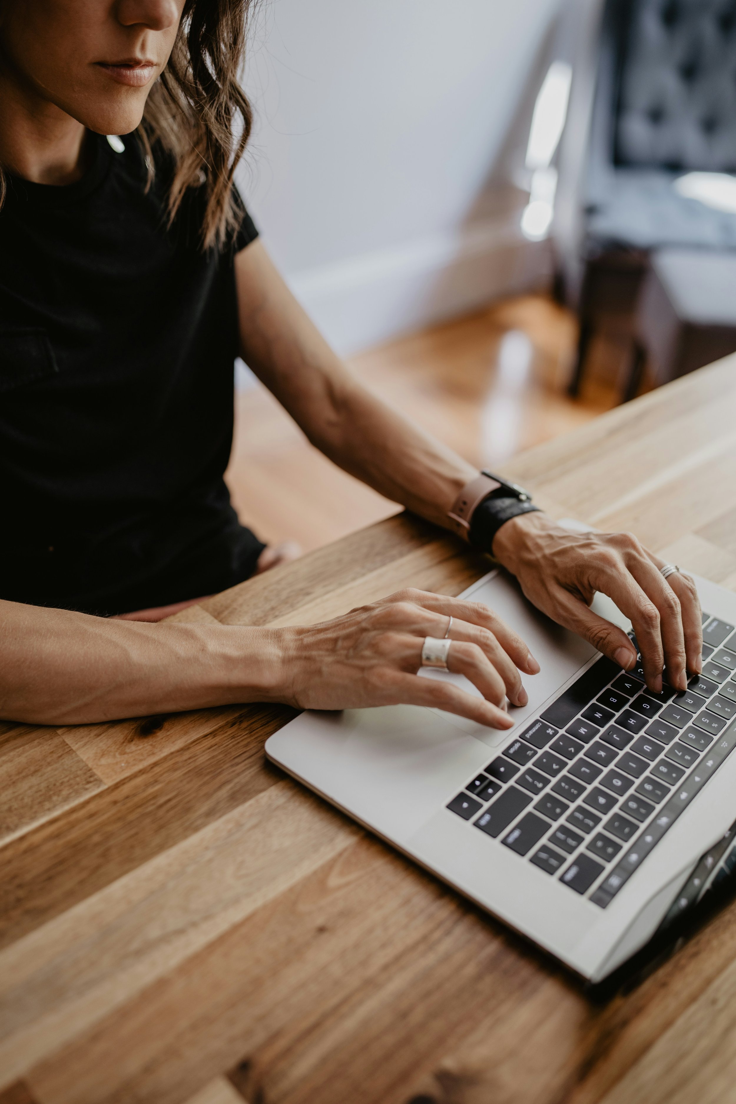 A woman's hands resting on a laptop at a wooden desk