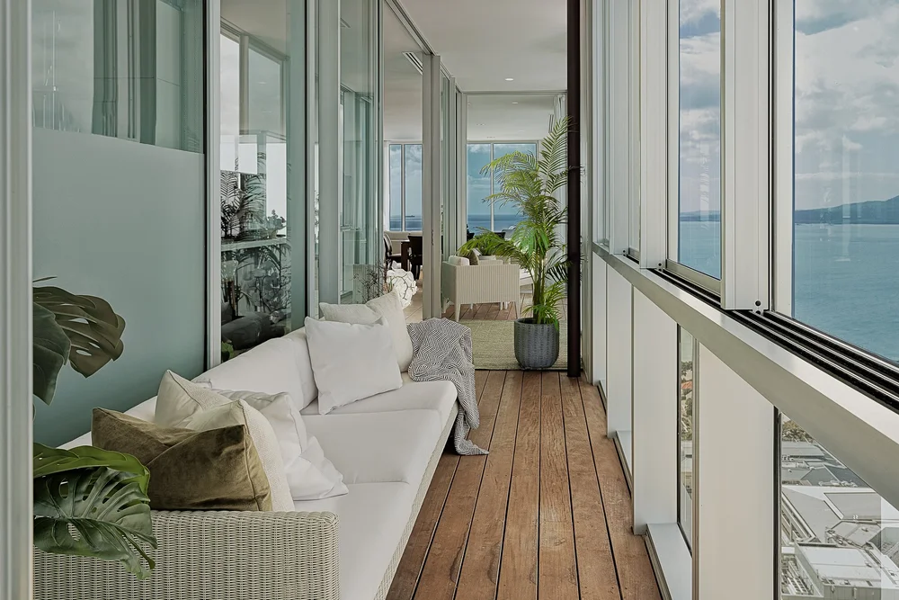 Sheltered balcony with pale seating, green cushions and timber flooring.