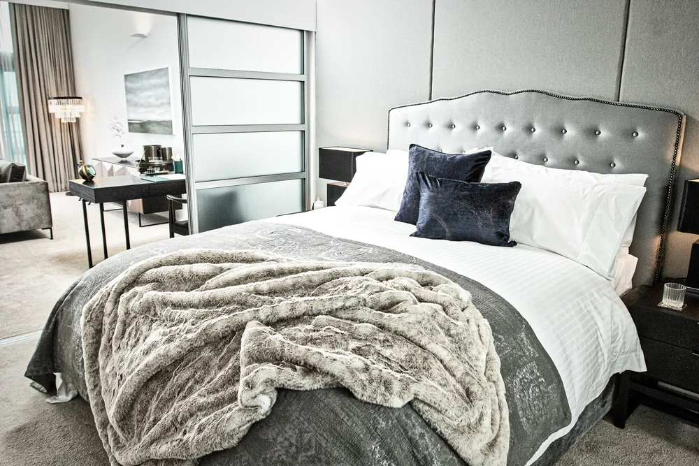 Bedroom with grey upholstered headboard and layered neutral bedding.