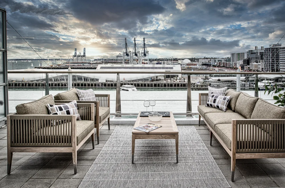 Waterfront balcony with woven seating, cushions and a low coffee table.