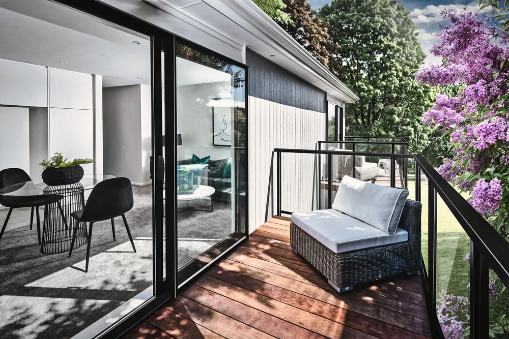 Compact timber balcony with outdoor chair beside sliding glass doors.