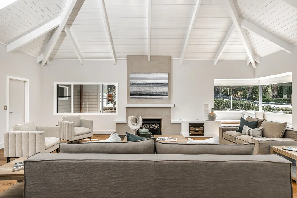 Sandspit living room with fireplace and exposed white roof beams.