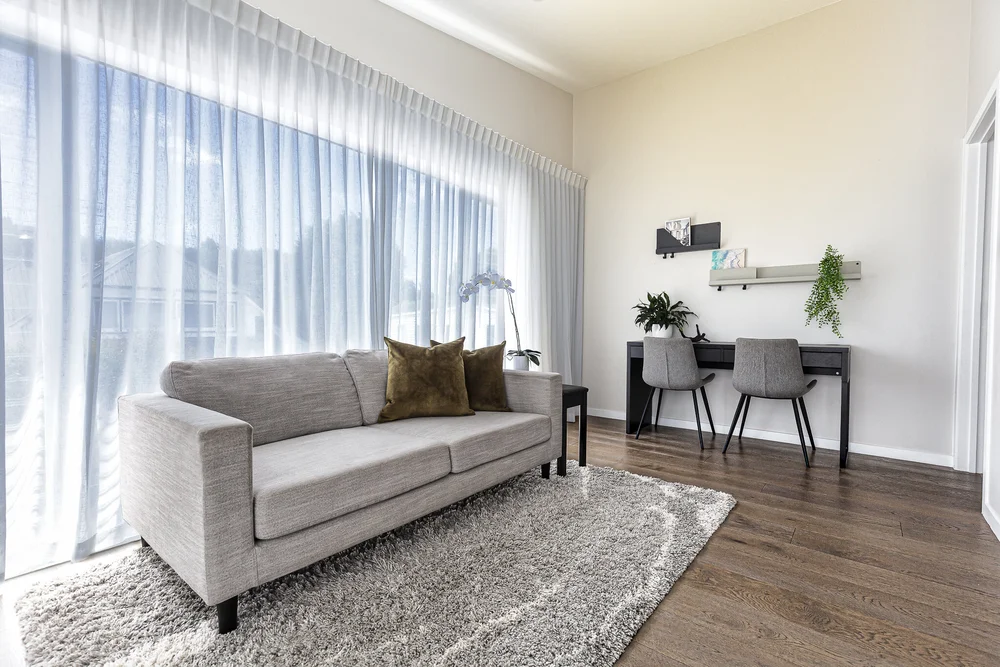 Pale sofa beside sheer drapes and a compact desk area.