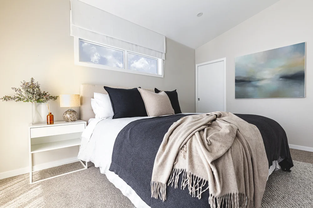 Kohimarama bedroom with white bedding, dark cushions, a soft throw and landscape artwork.