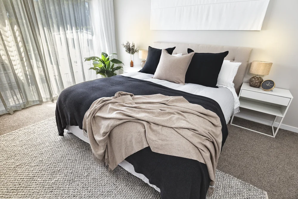 Softly lit bedroom with layered bedding and full-height drapes.