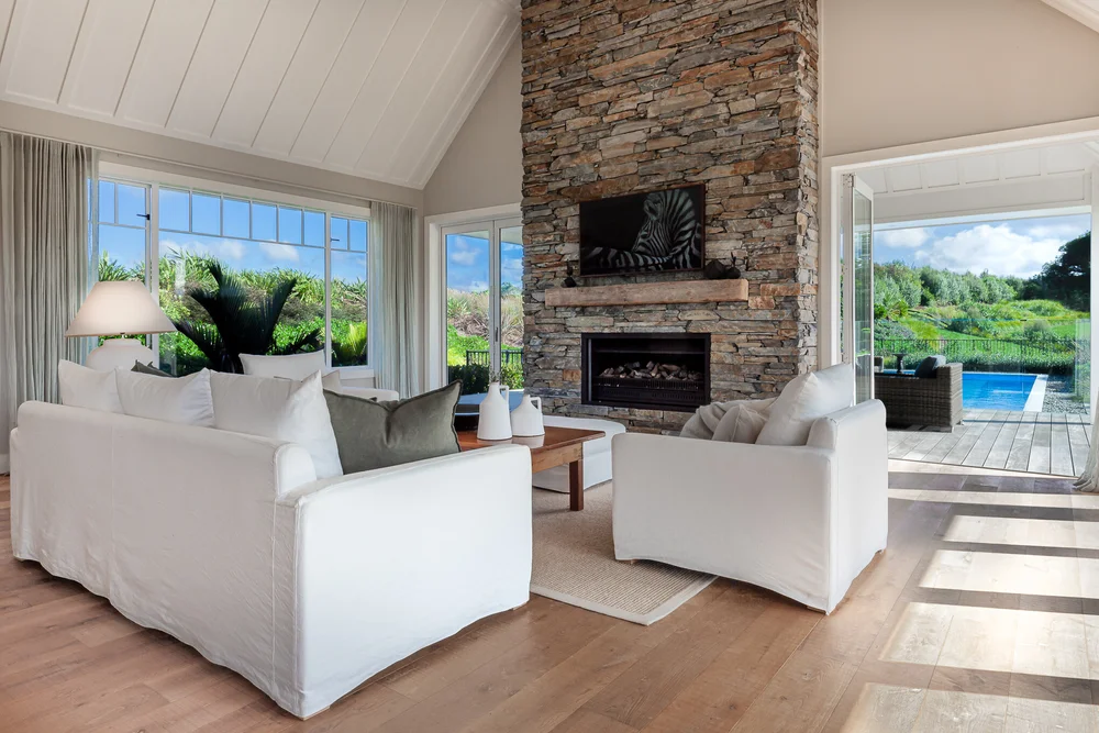 Matakana living room with stone fireplace and doors opening towards the pool.