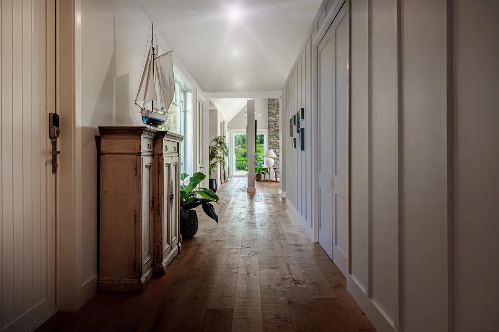 Long hallway with grey panelling, timber floor and antique-style cabinet.