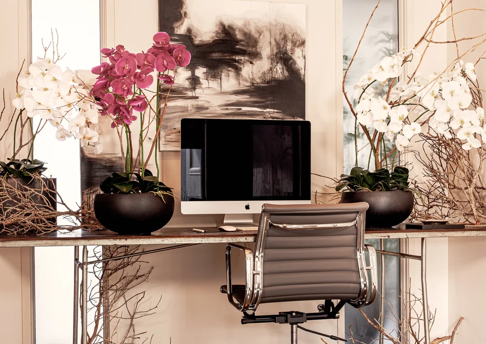 Home office desk with orchids, artwork and a leather office chair.