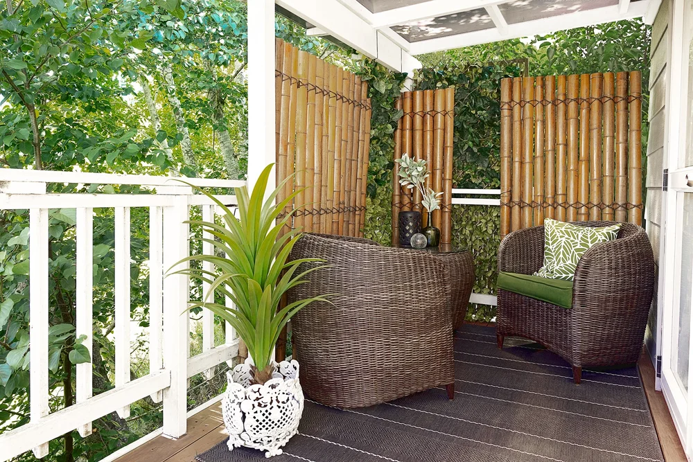 Covered outdoor nook with woven chairs and lush plants.