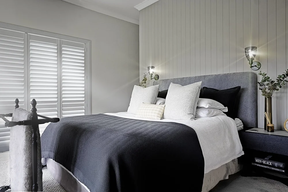 Bedroom with white bedding, dark accents and plantation shutters.
