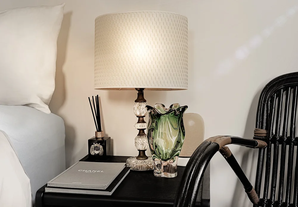 Bedside lamp and decorative glassware beside a dark chair.
