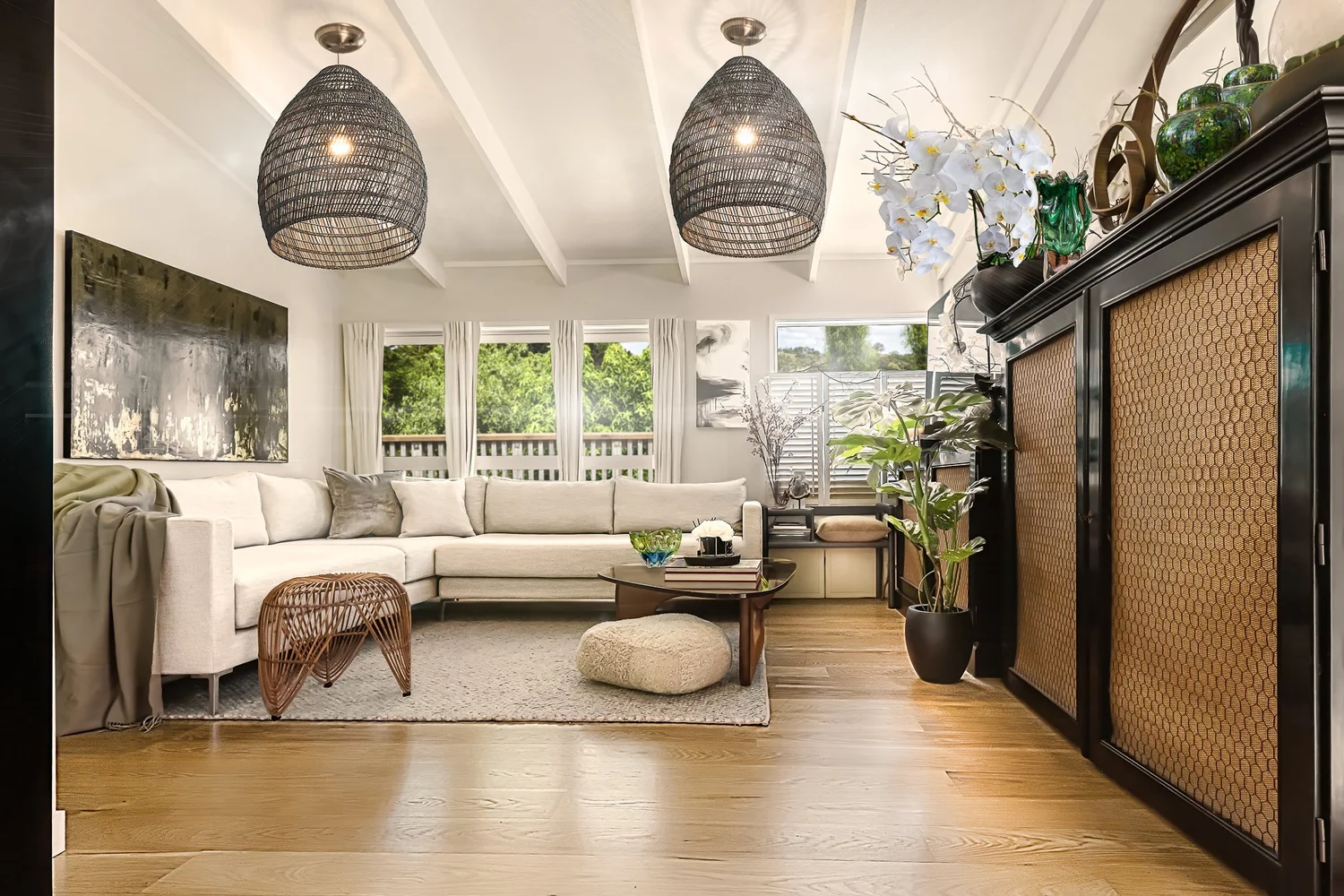 Farmhouse living room with pale seating, woven pendants and dark cabinetry.