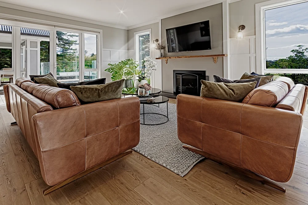 Leather seating arranged around a fireplace beside large windows.