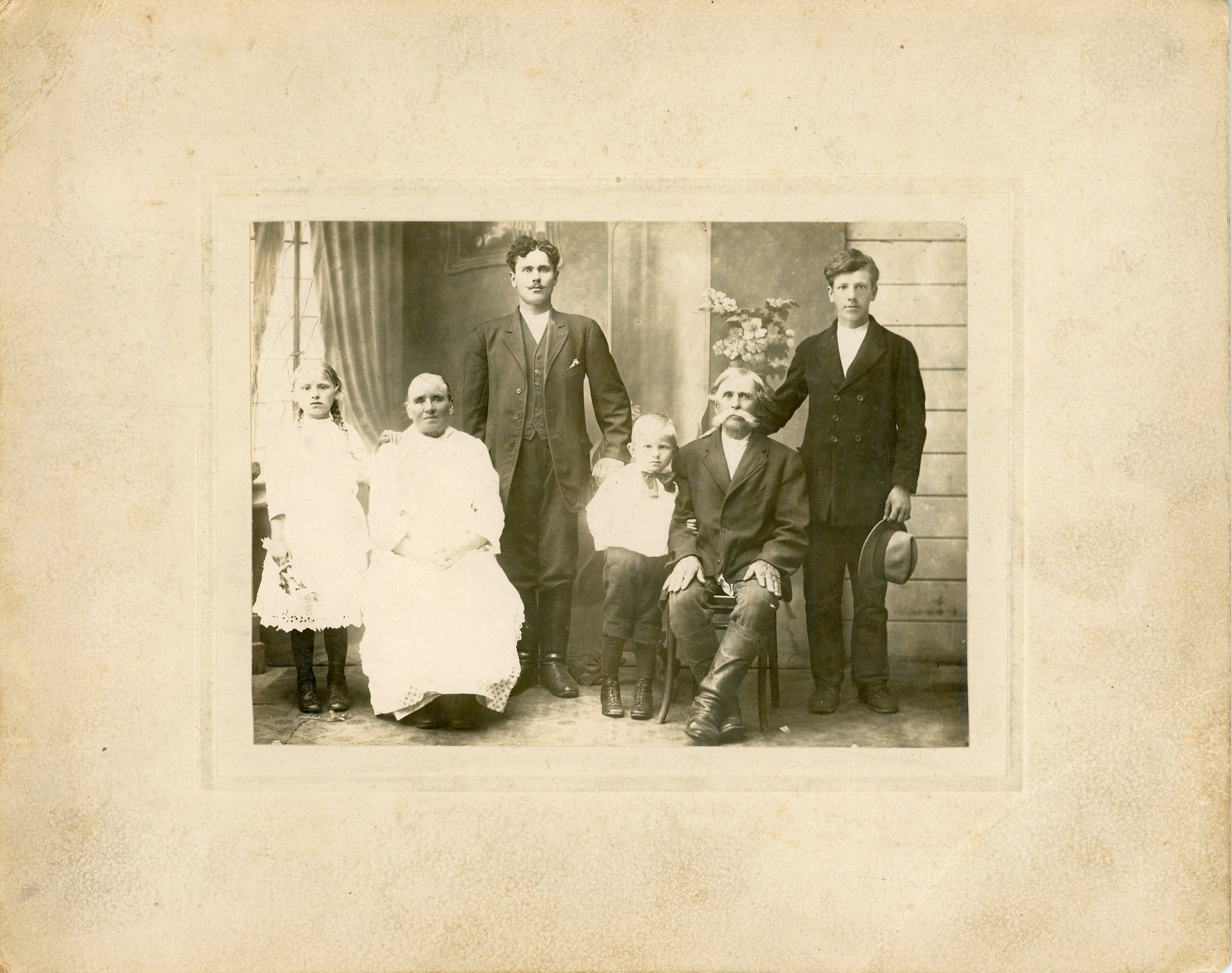 Vintage family portrait, six people, early 20th century fashion, seated and standing poses, neutral background.