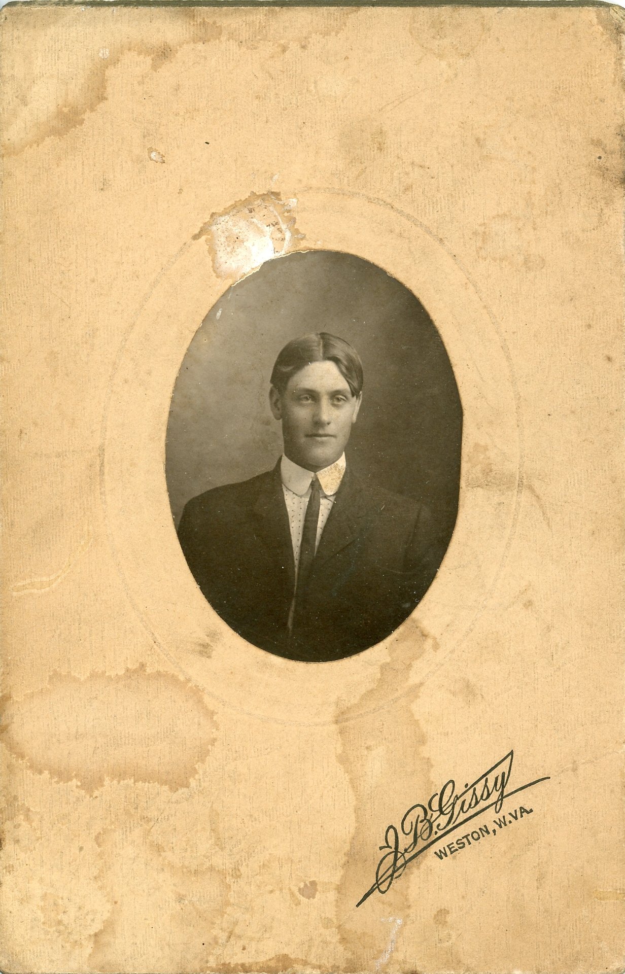 Vintage portrait of a man in a suit with a sepia tone, mounted on an aged cardboard with "J.P. Grissy, Weston, W.VA" printed on it.