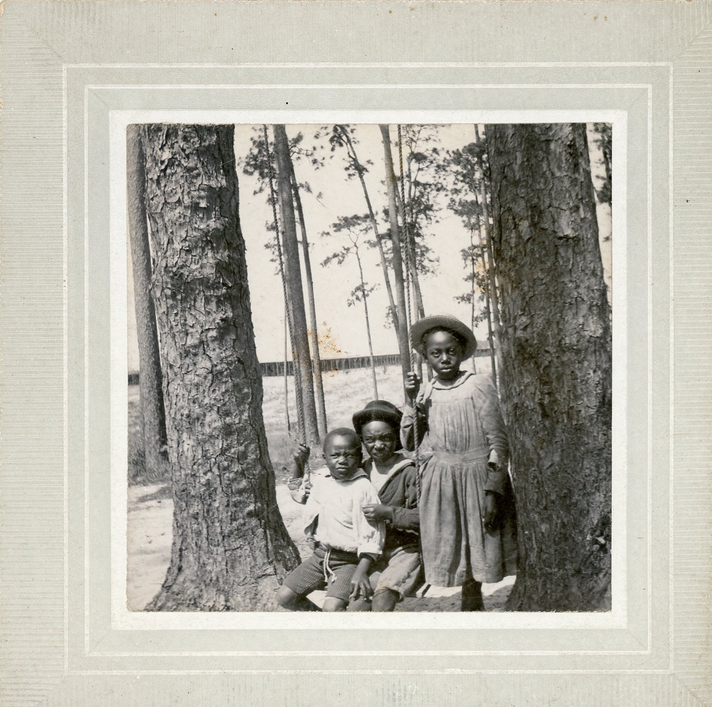 Vintage photo of three children posing outdoors among trees.