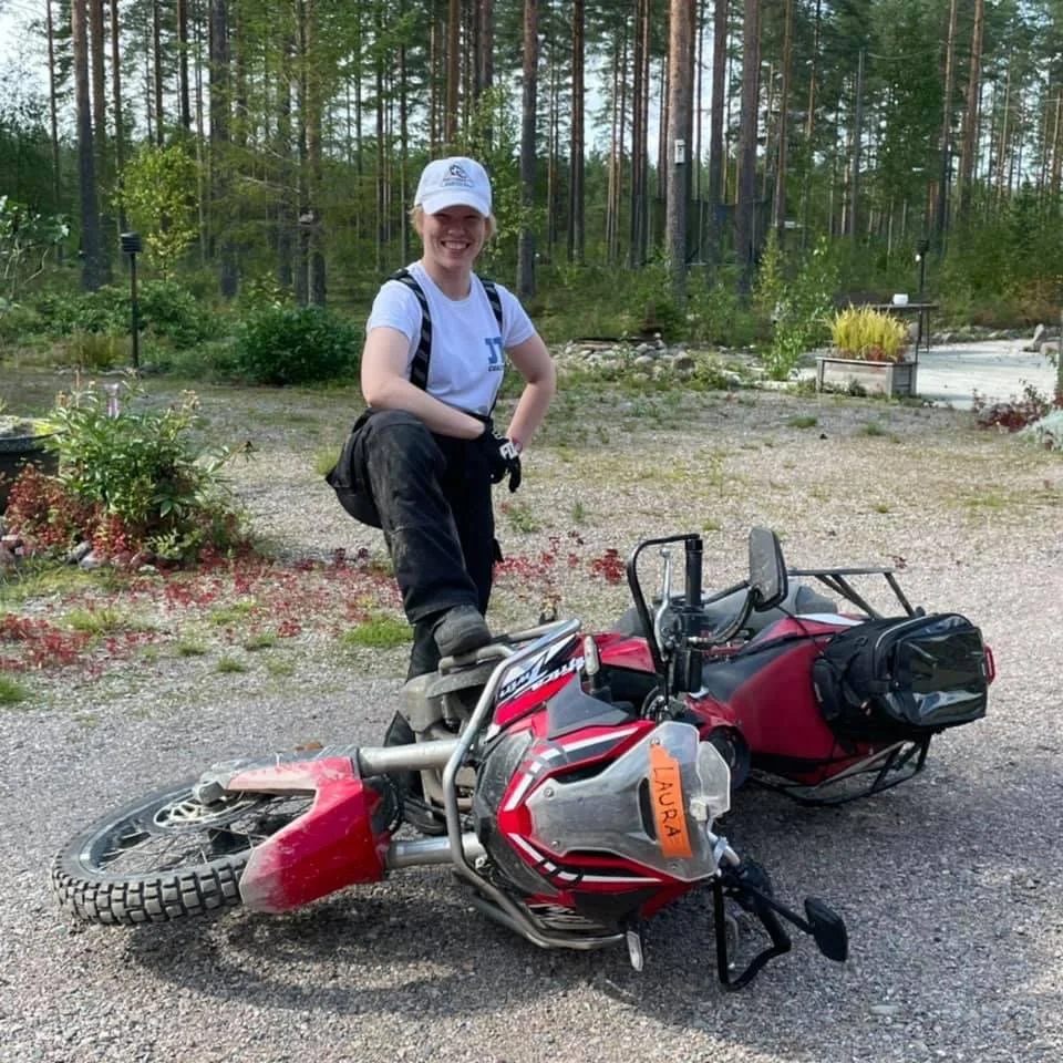 Hymyilevä nainen seisoo maastokopterin ja matkailuvälineiden vieressä metsäisessä ympäristössä.