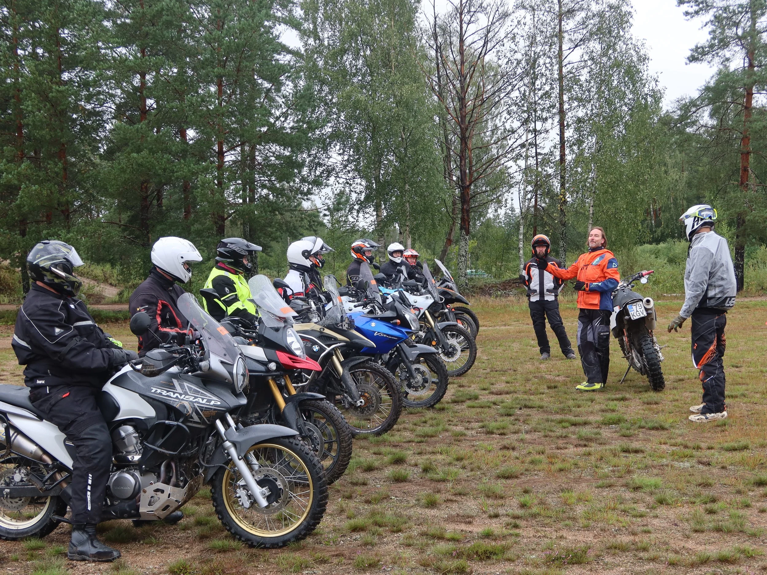 Ryhmän motocross-puuhat luonnon keskellä, useita motorisoituja ajoneuvoja ja ihmiset varusteissaan.