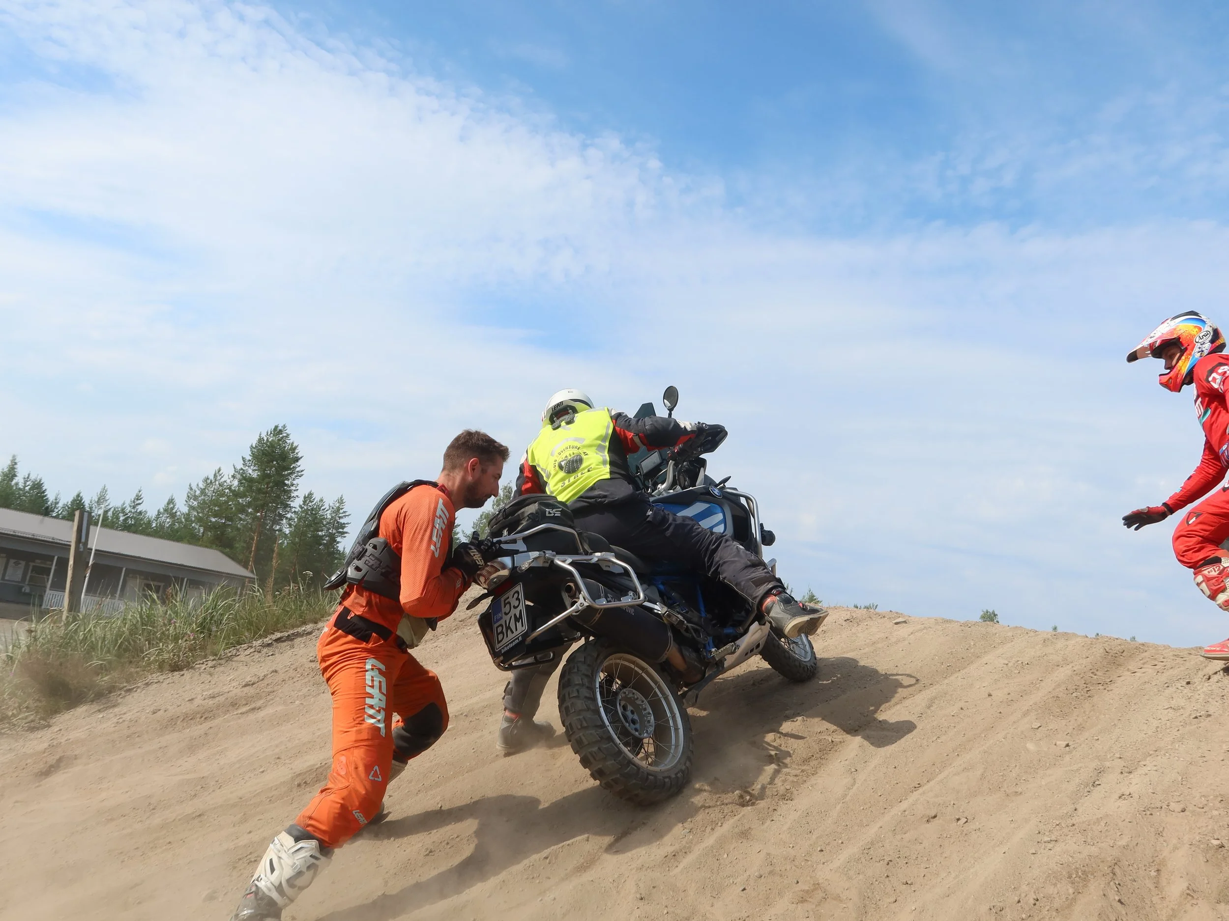 Motorcross-kuski kaatumassa pystyynkuulmassa, apuvoimia yrittämässä auttaa kaatunutta motocrossia.