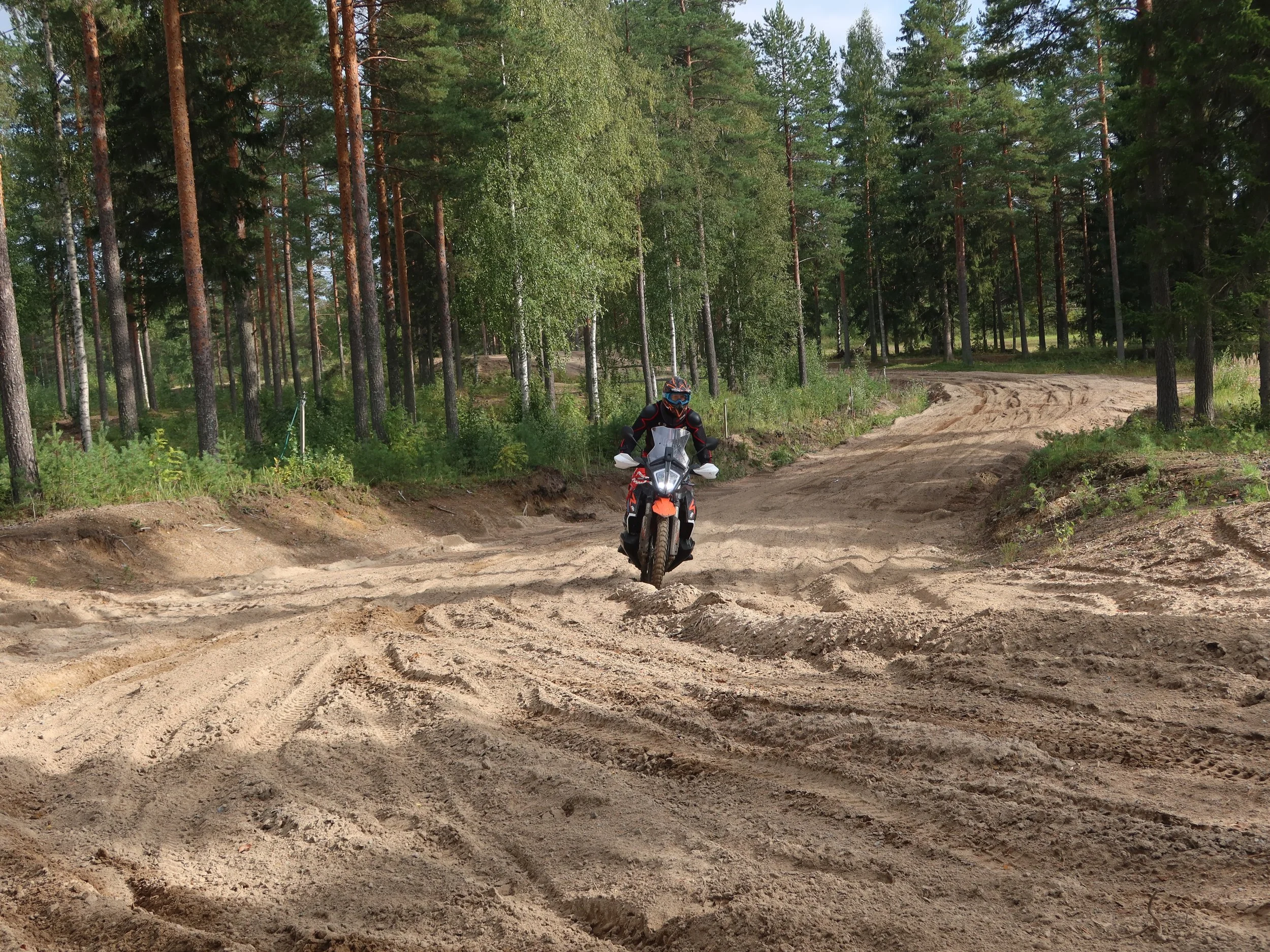 Mies ajaa motocross-pyörällä hiekkatiellä metsän keskellä.