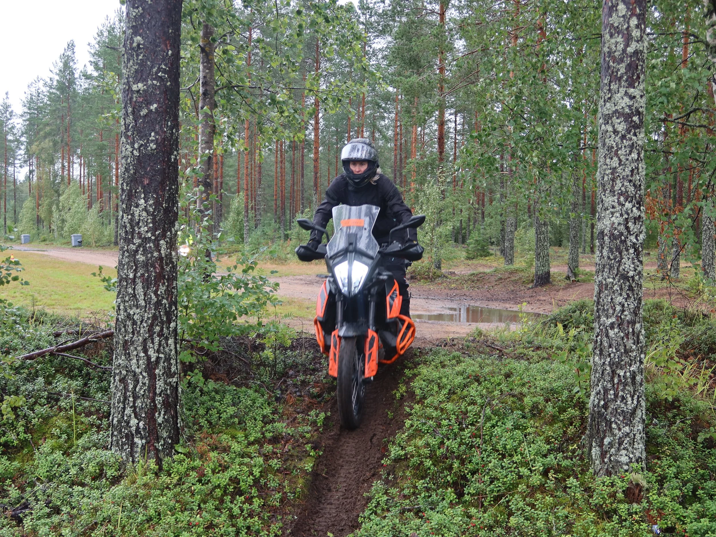 Mies moottoripyöräilemässä metsässä siirtymässä polulta pienen kuoppaisen ja mutaisen rinteen yli.