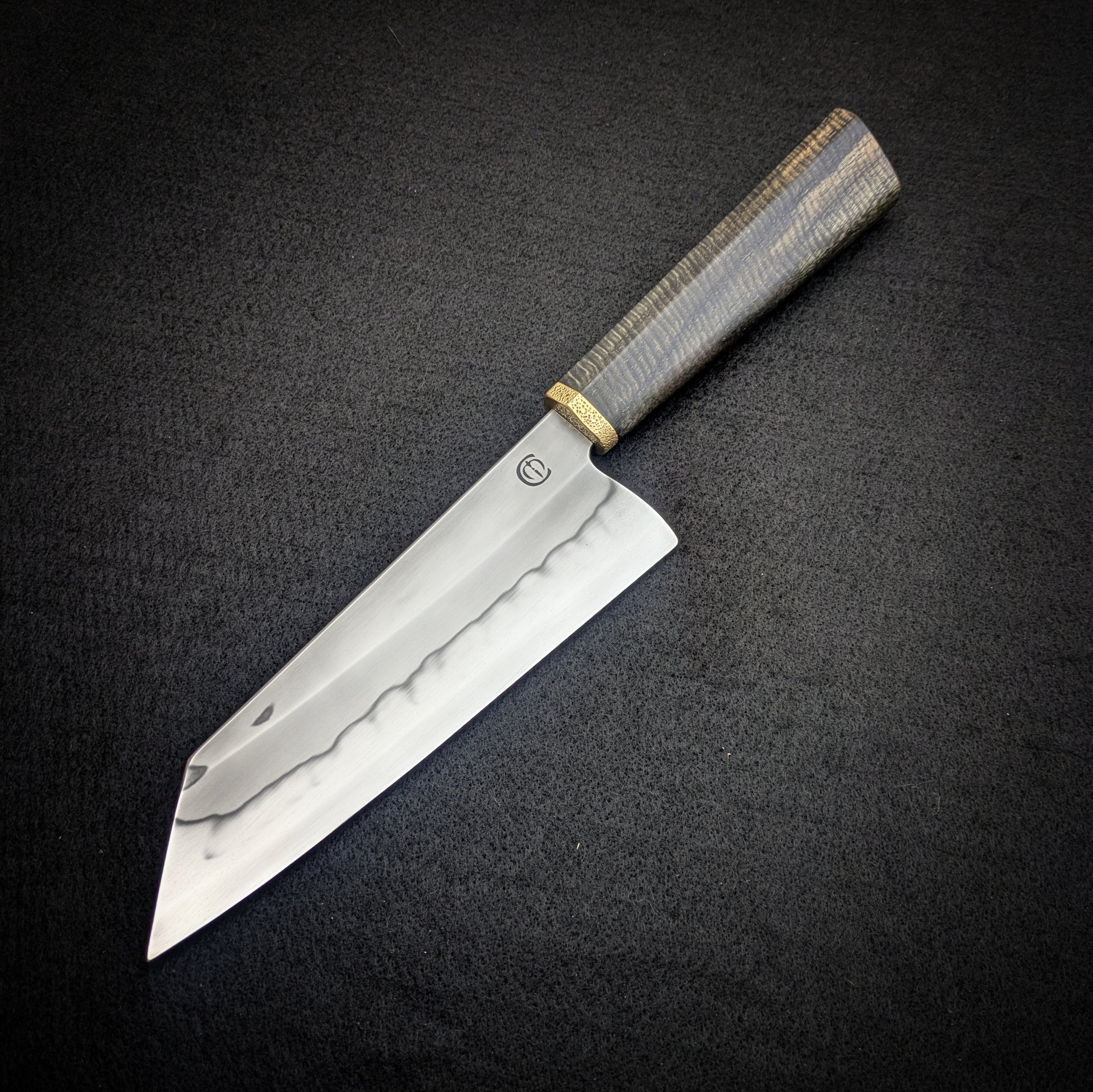 A kitchen knife with a patterned handle and a brass bolster placed on a dark countertop.