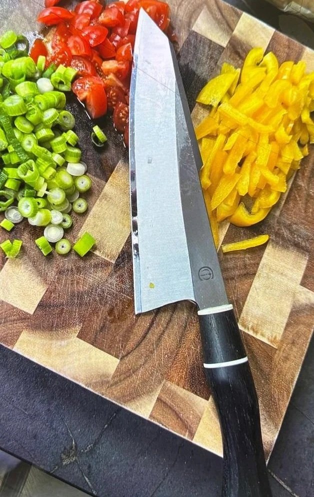 Chopped tomatoes, sliced green onions, and sliced yellow bell peppers on a wooden cutting board with a large chef's knife.