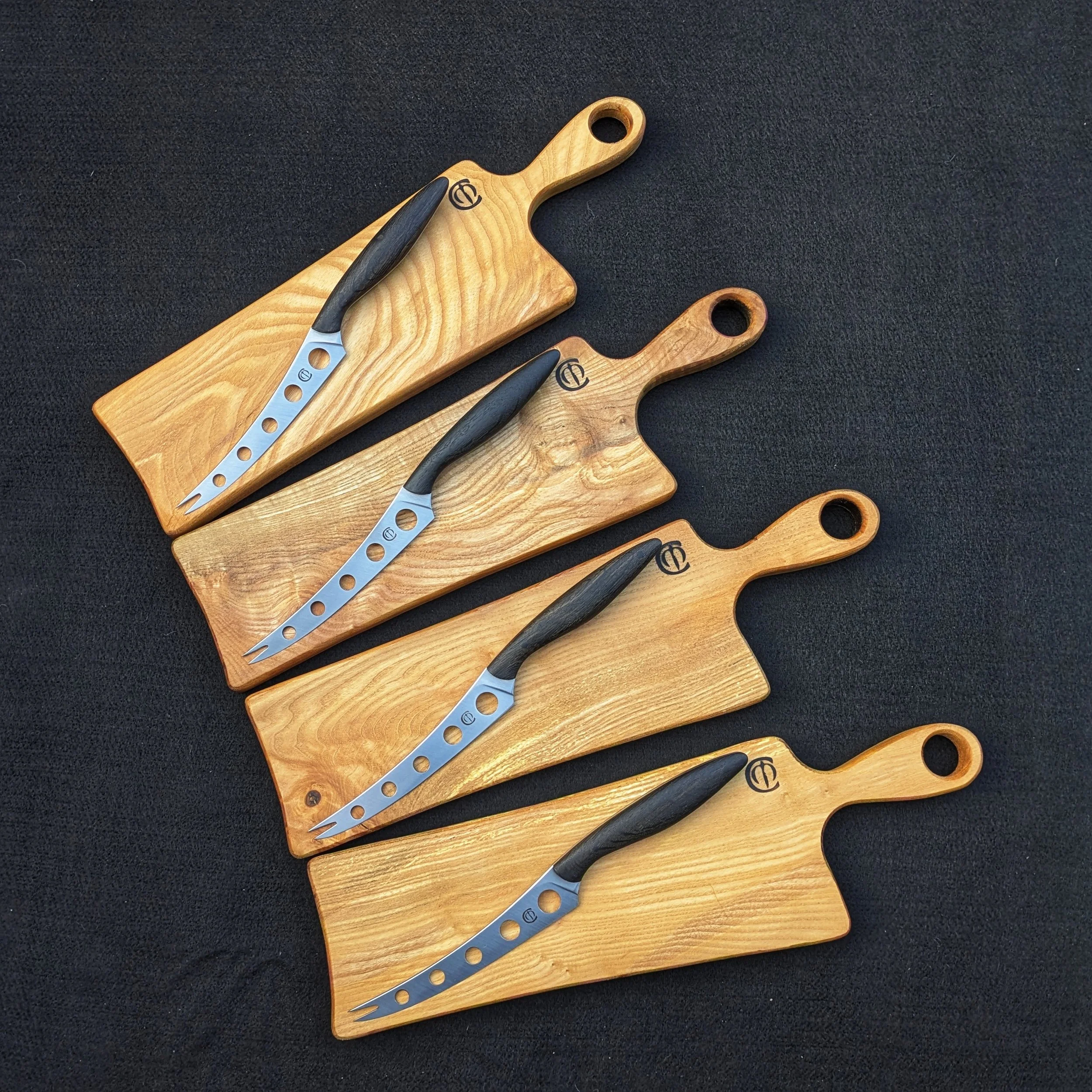 Four wooden cutting boards with black-handled cheese knives on a black surface.