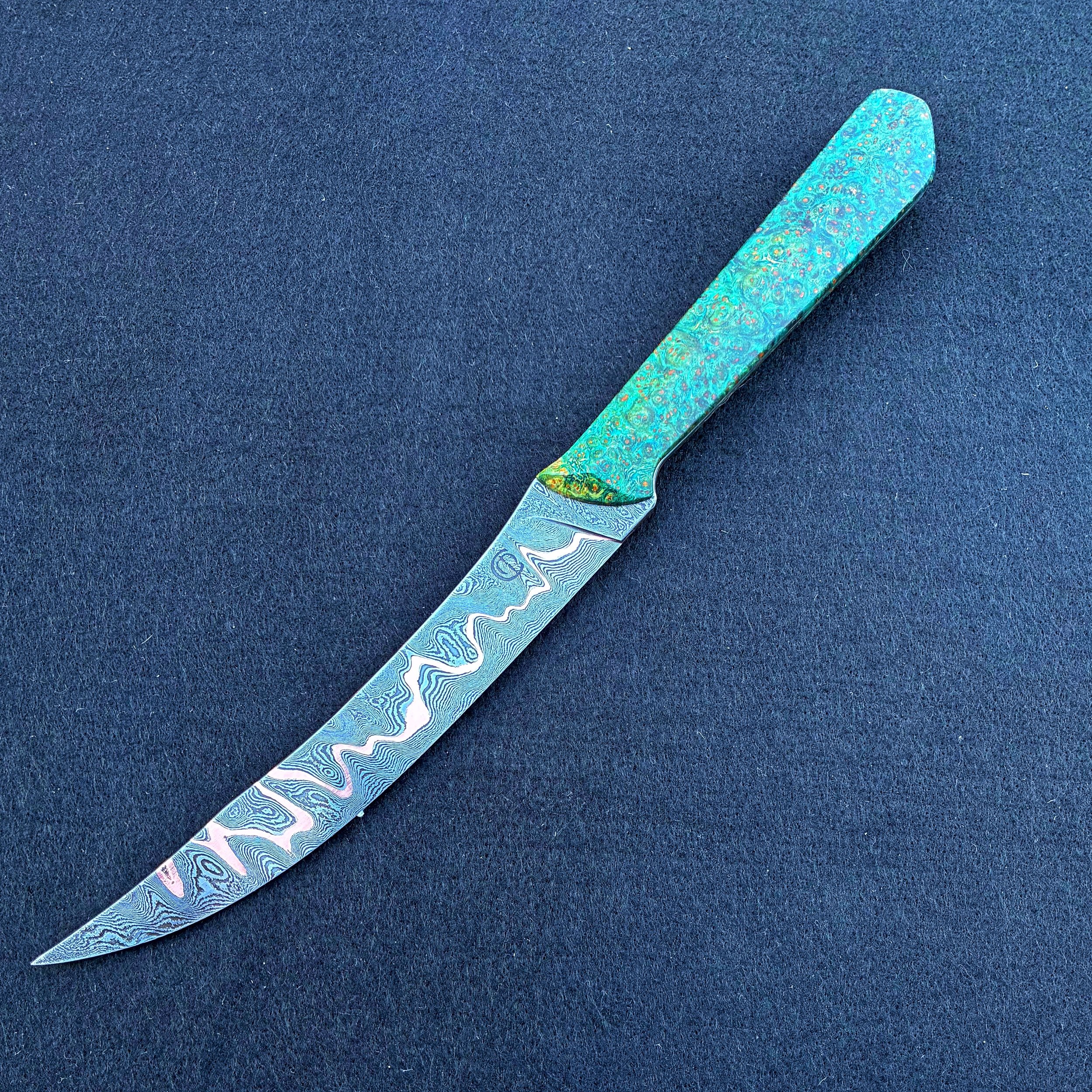 Colorful knife with a Damascus steel blade, resting on a dark blue background.