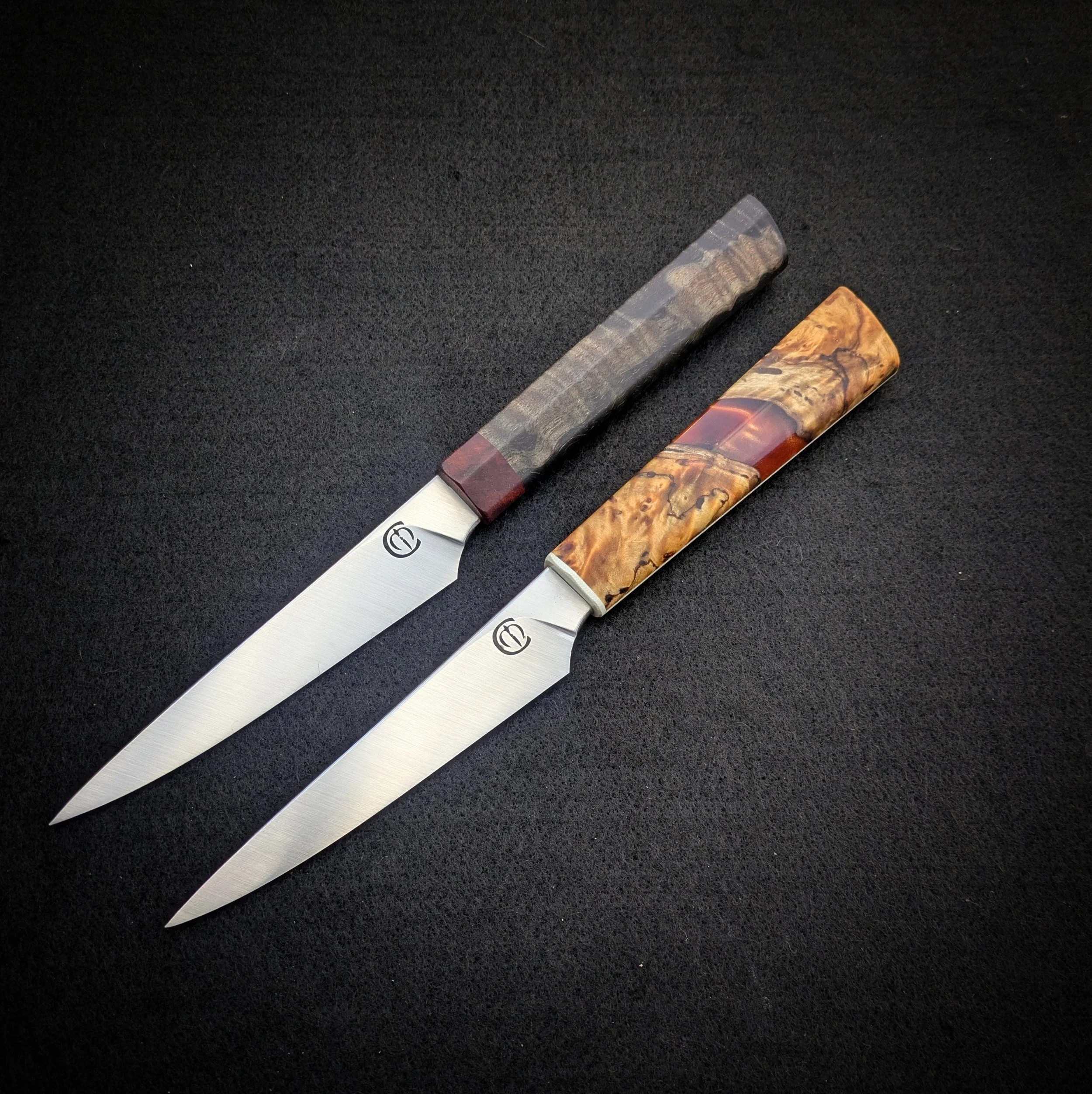 A pair of table knives with handles of a wood grain pattern, placed on a dark textured surface.