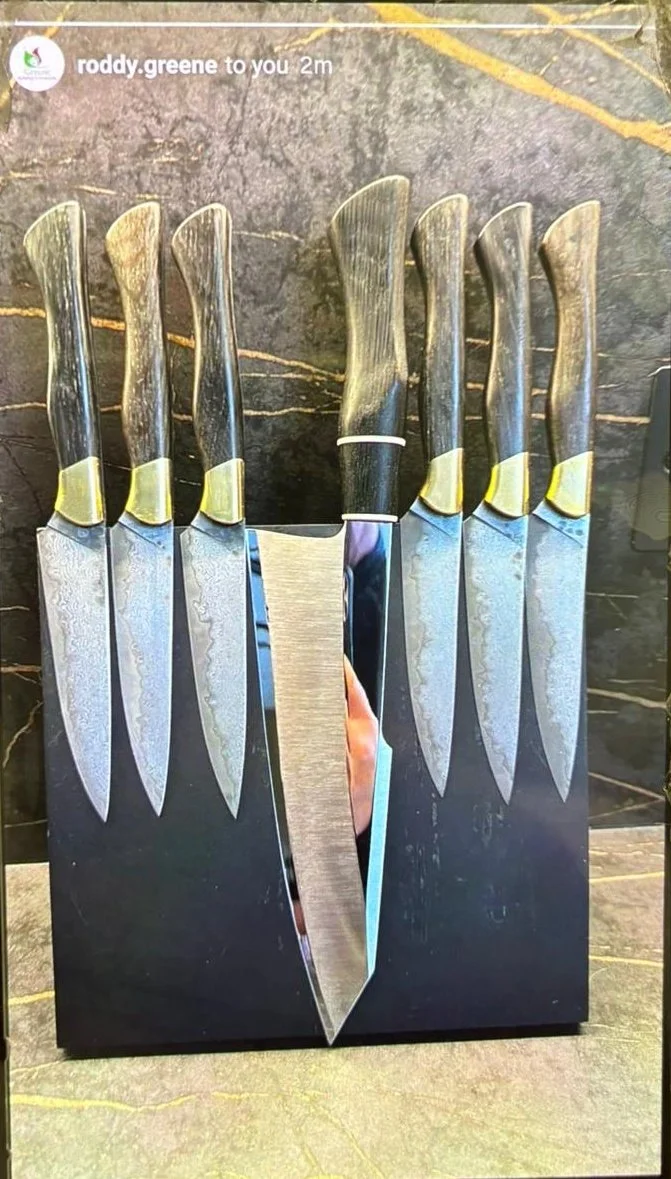 Display of seven kitchen knives with wooden handles arranged in a row, with a large knife in the center, set against a black marble background.