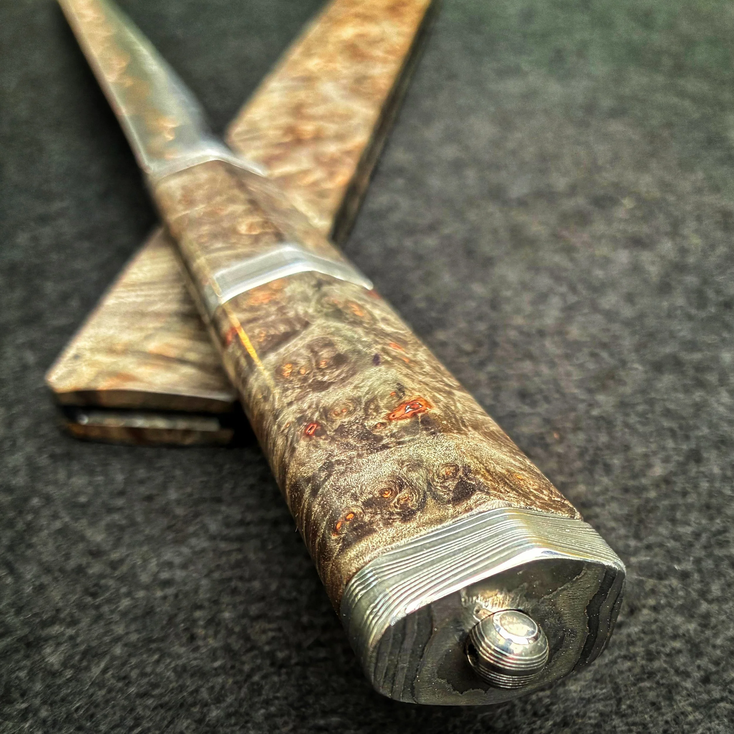 Close-up of a knife with a wood grain pattern on the handle, lying on a dark surface.