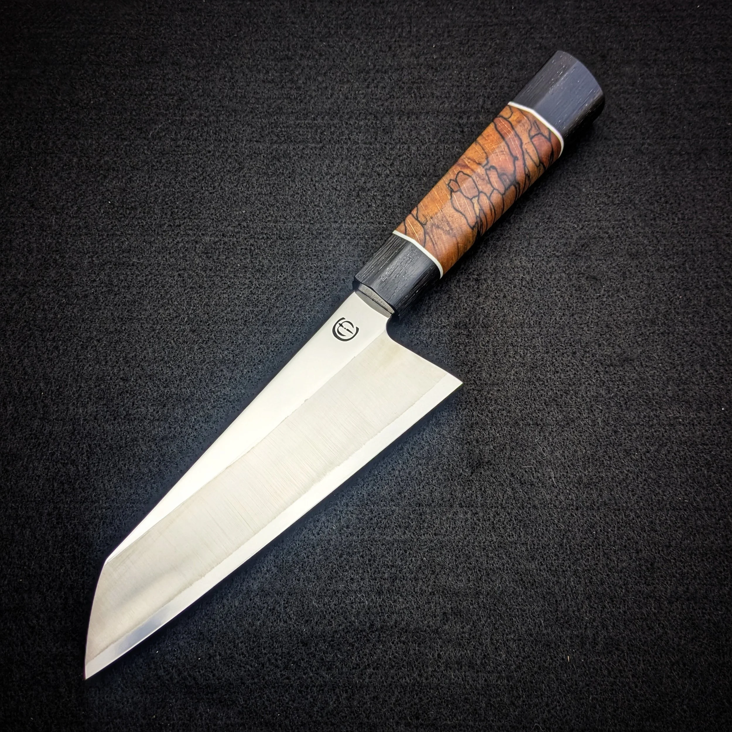 Close-up of a chef's knife with a patterned handle on a black textured surface.