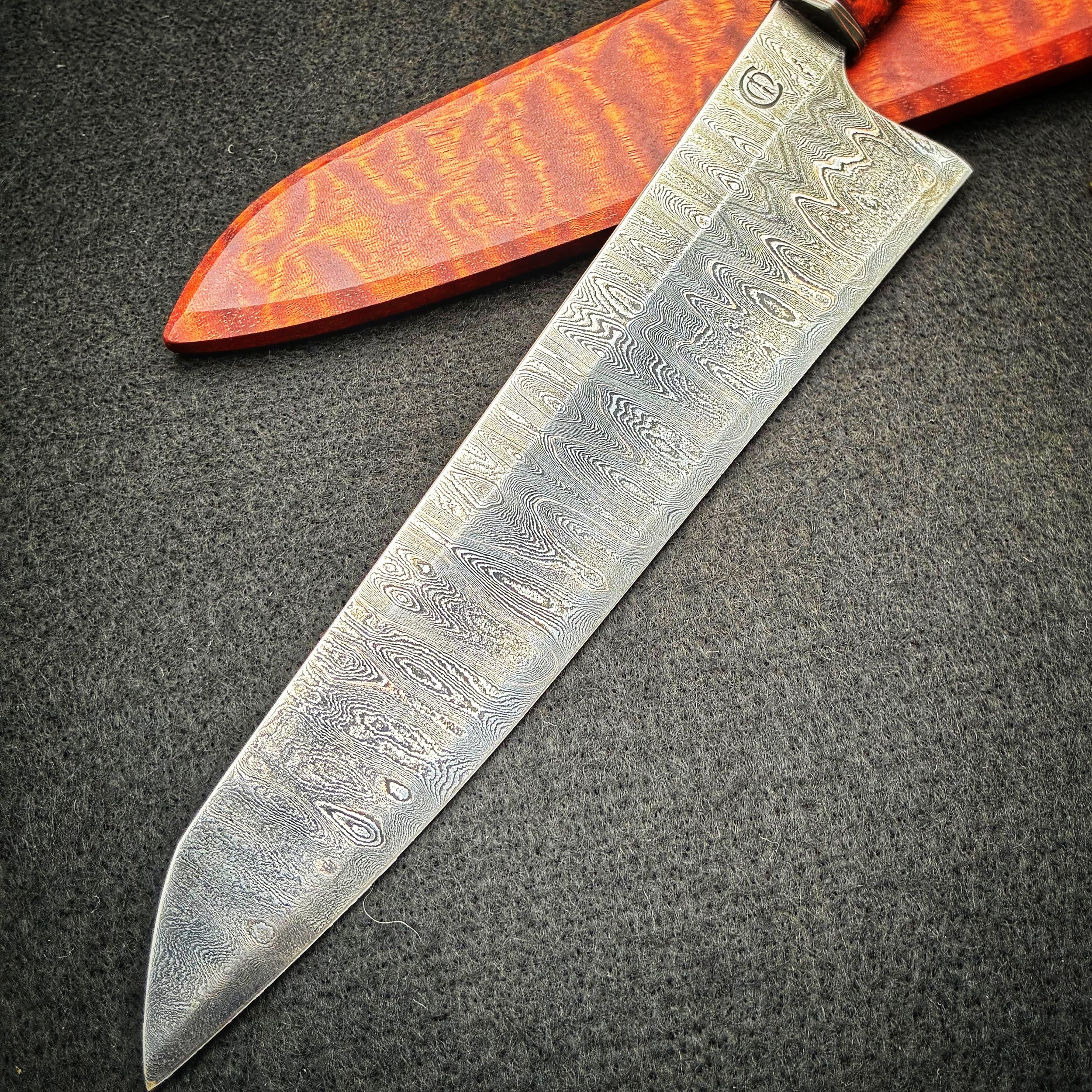 A Damascus steel kitchen knife with intricate wave patterns on the blade, resting on a textured black surface, partially inside a wooden sheath.