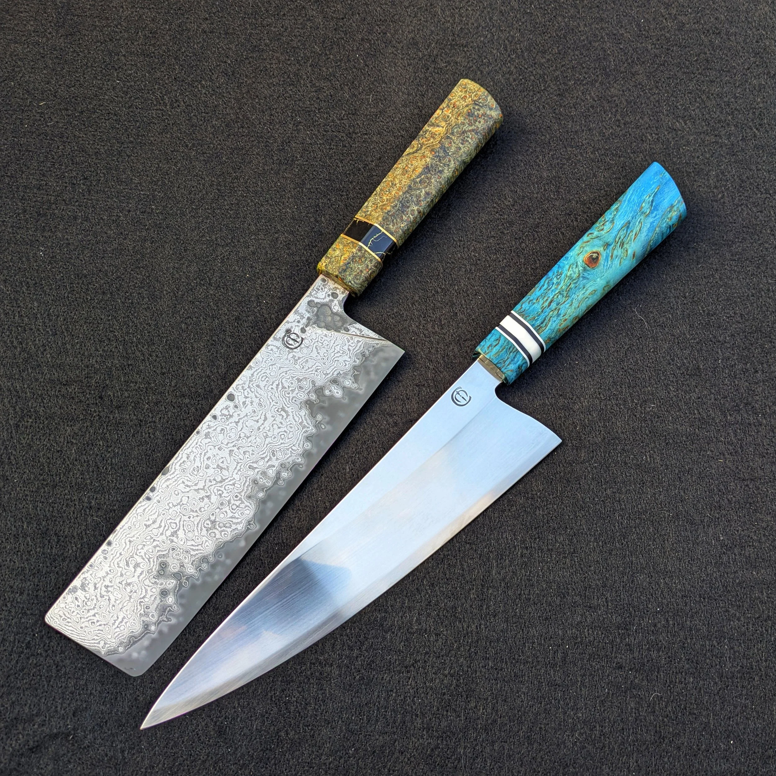 Two chef knives with patterned handles and distinct blades, one with a damascus pattern and the other with a plain, shiny finish, laid out on a black surface.