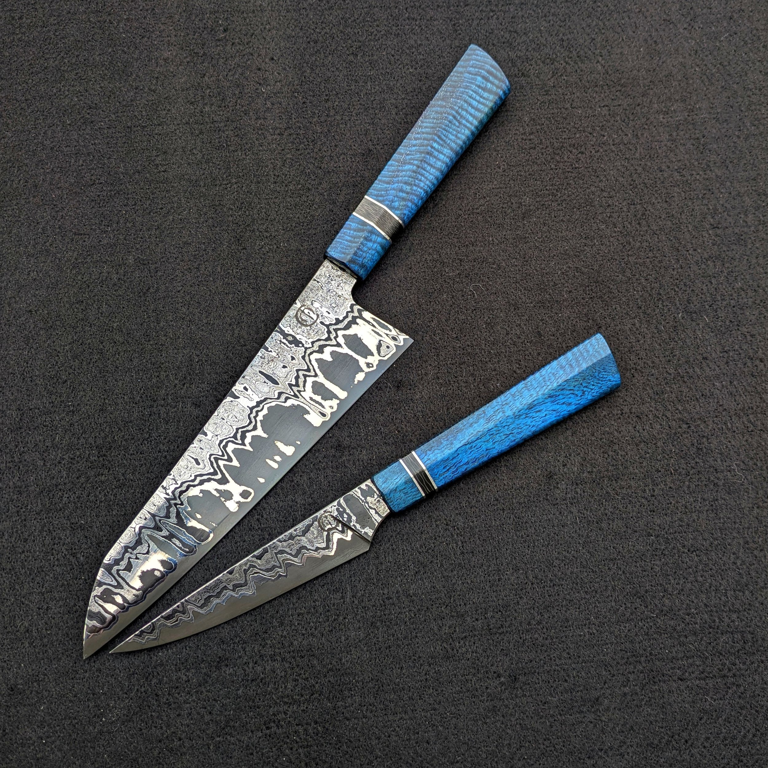 Two patterned knives with blue handles on a black surface.