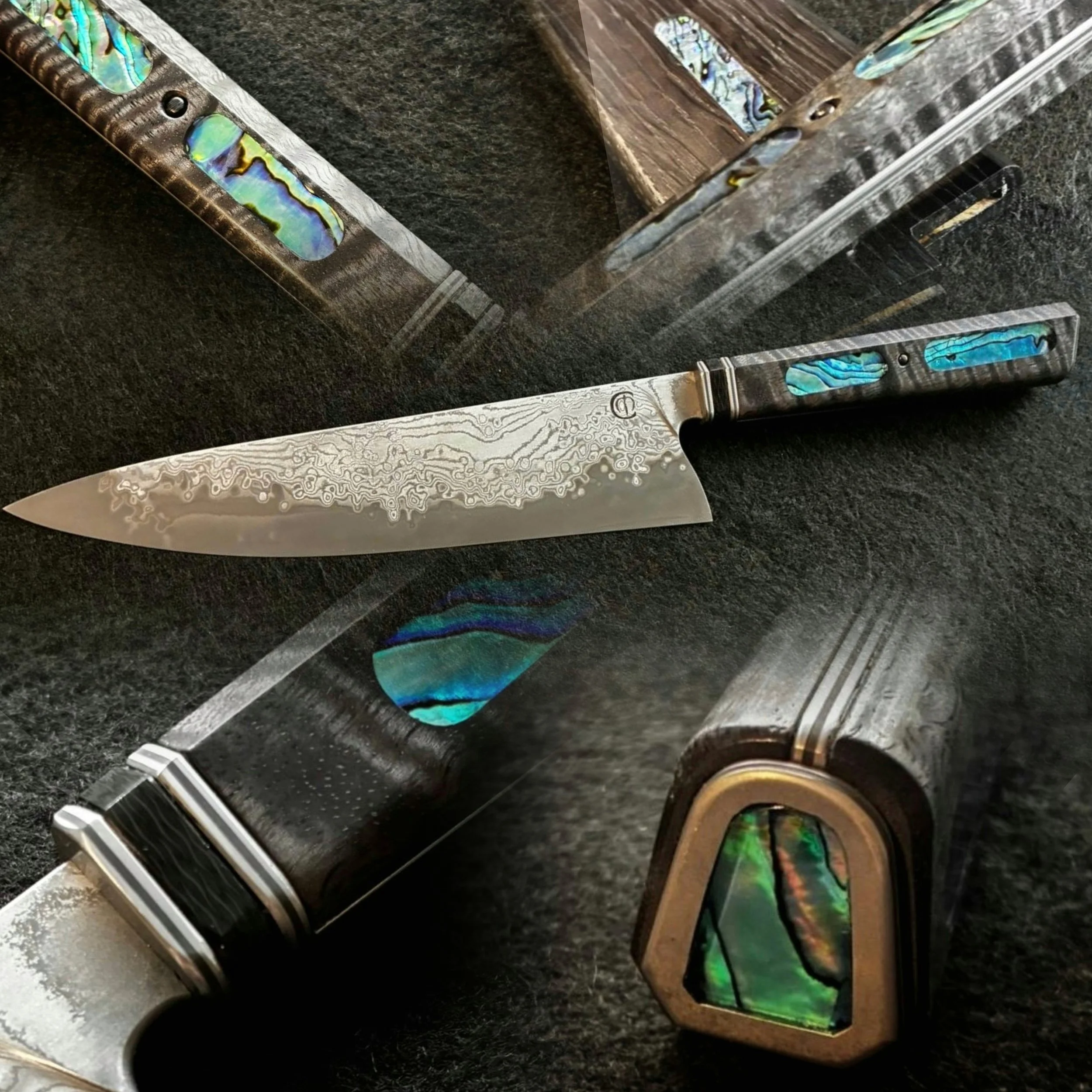 	
A VG10 Suminagashi steel kitchen knife with a patterned blade and a handle that has mother of pearl inlays, placed on a black textured surface
