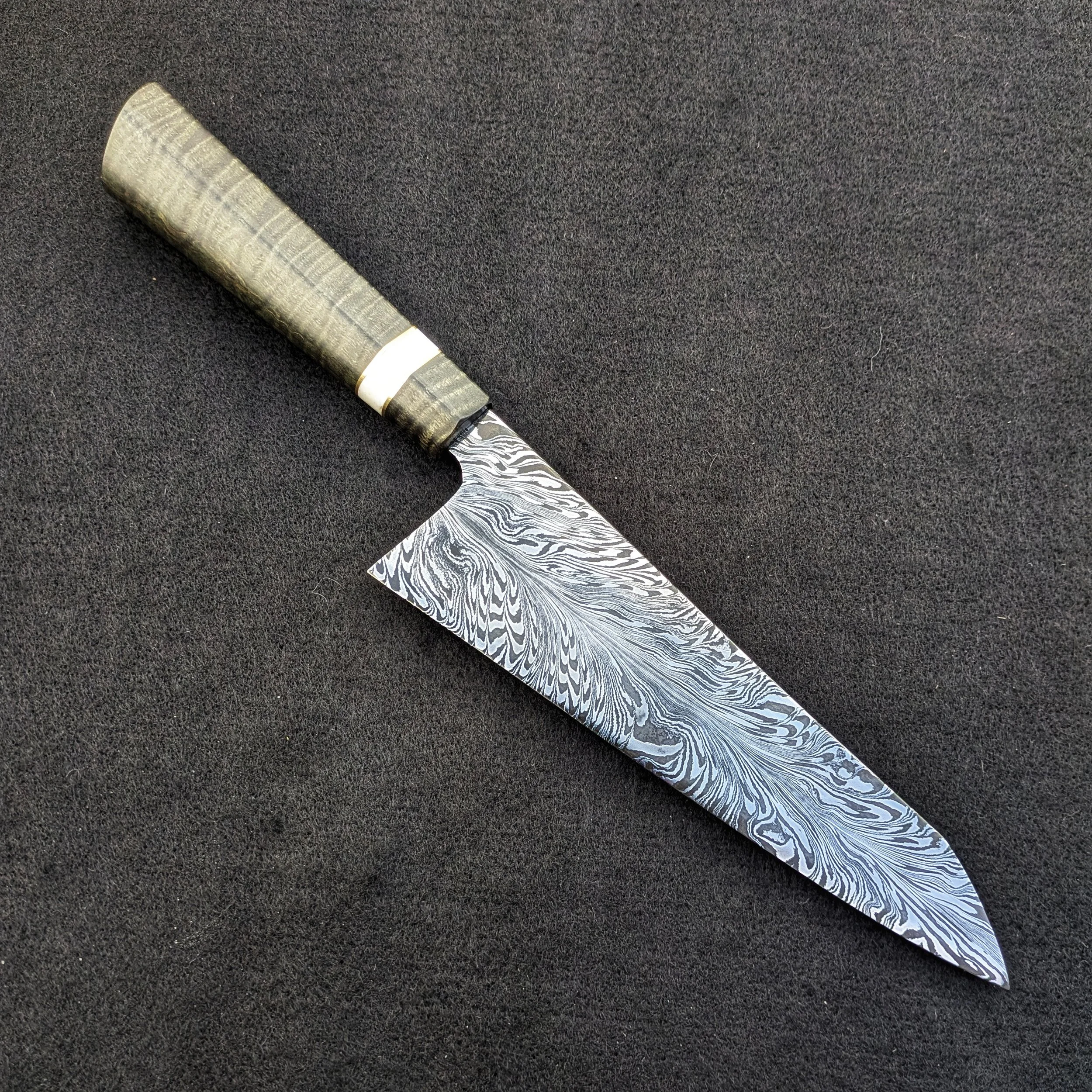 A Damascus steel kitchen knife with a patterned blade and a greenish handle on a black surface.