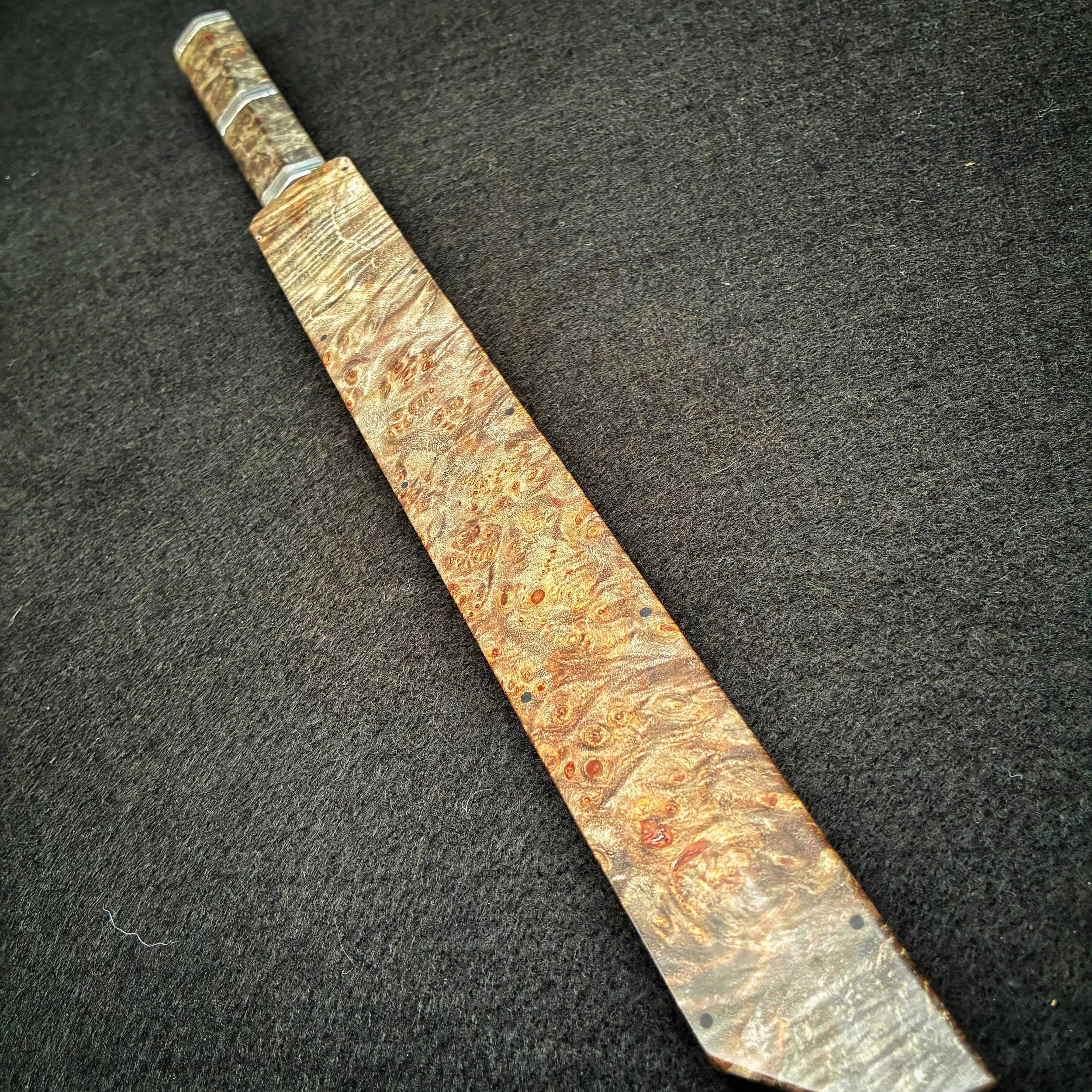 Close-up of a knife with a handle and blade made from a piece of polished, patterned wood or exotic material, resting on a black surface.