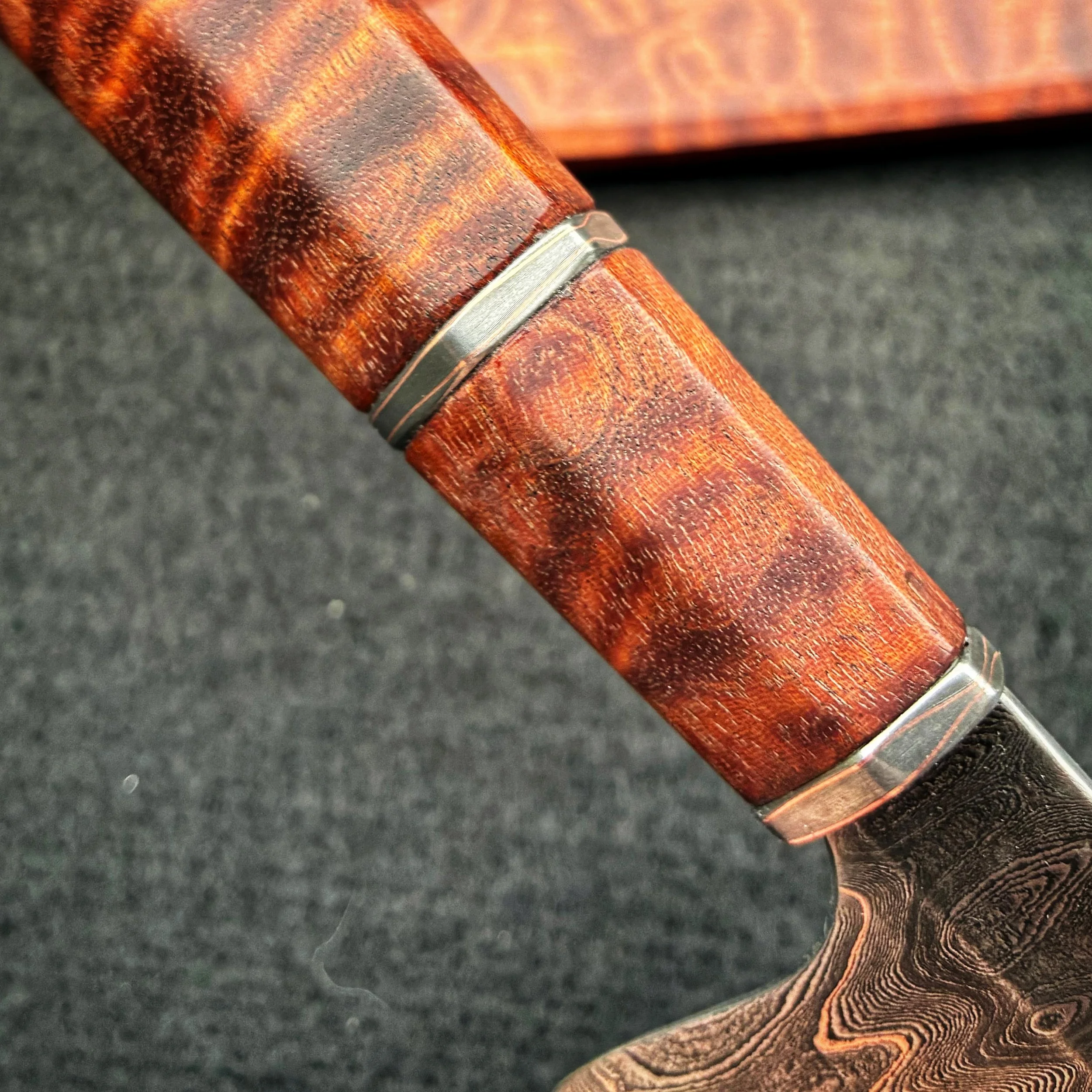 Close-up of a chef knife with a polished, textured grip and decorative metal bands, resting on a dark surface.