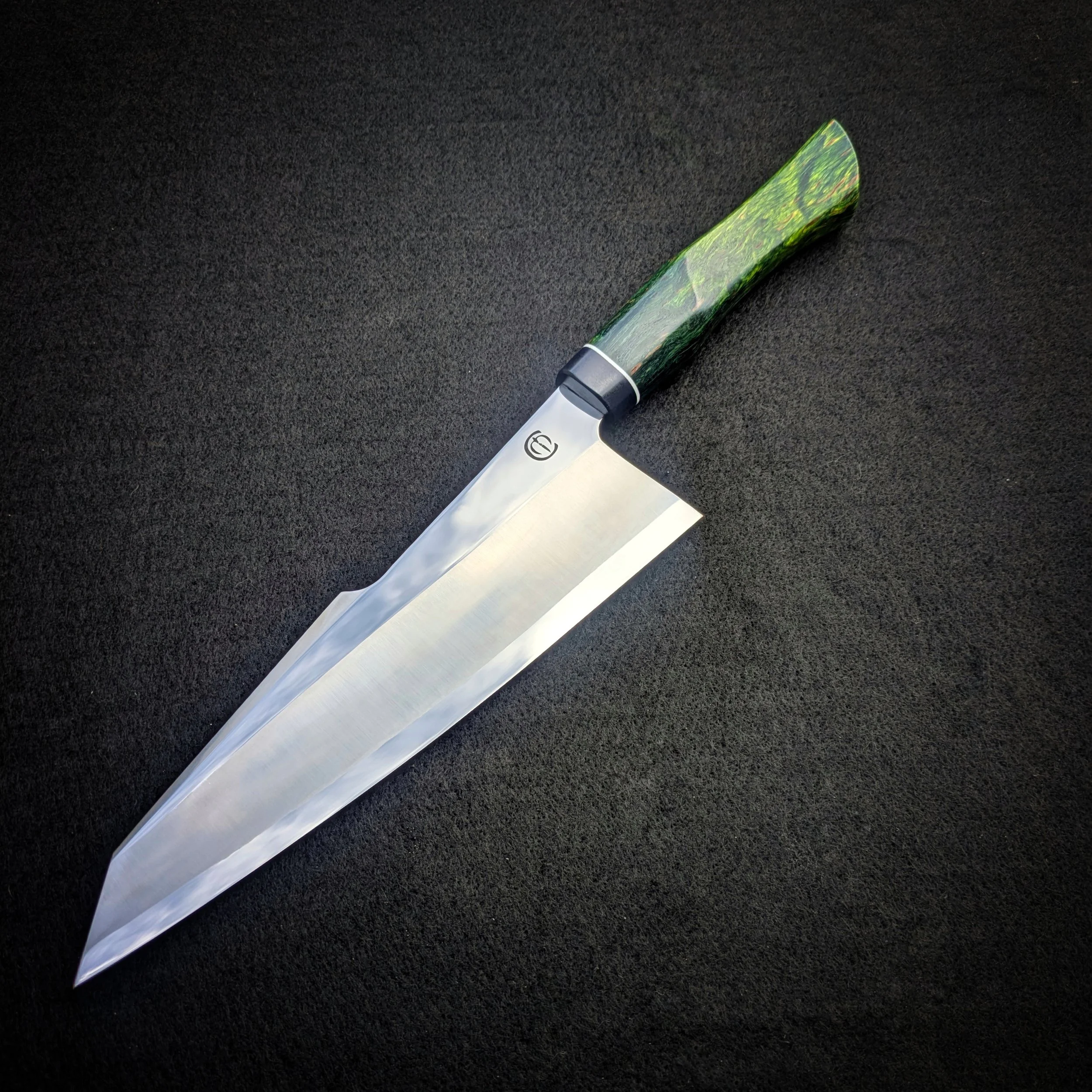 A chef's knife with a marbled green and black handle on a black textured surface.