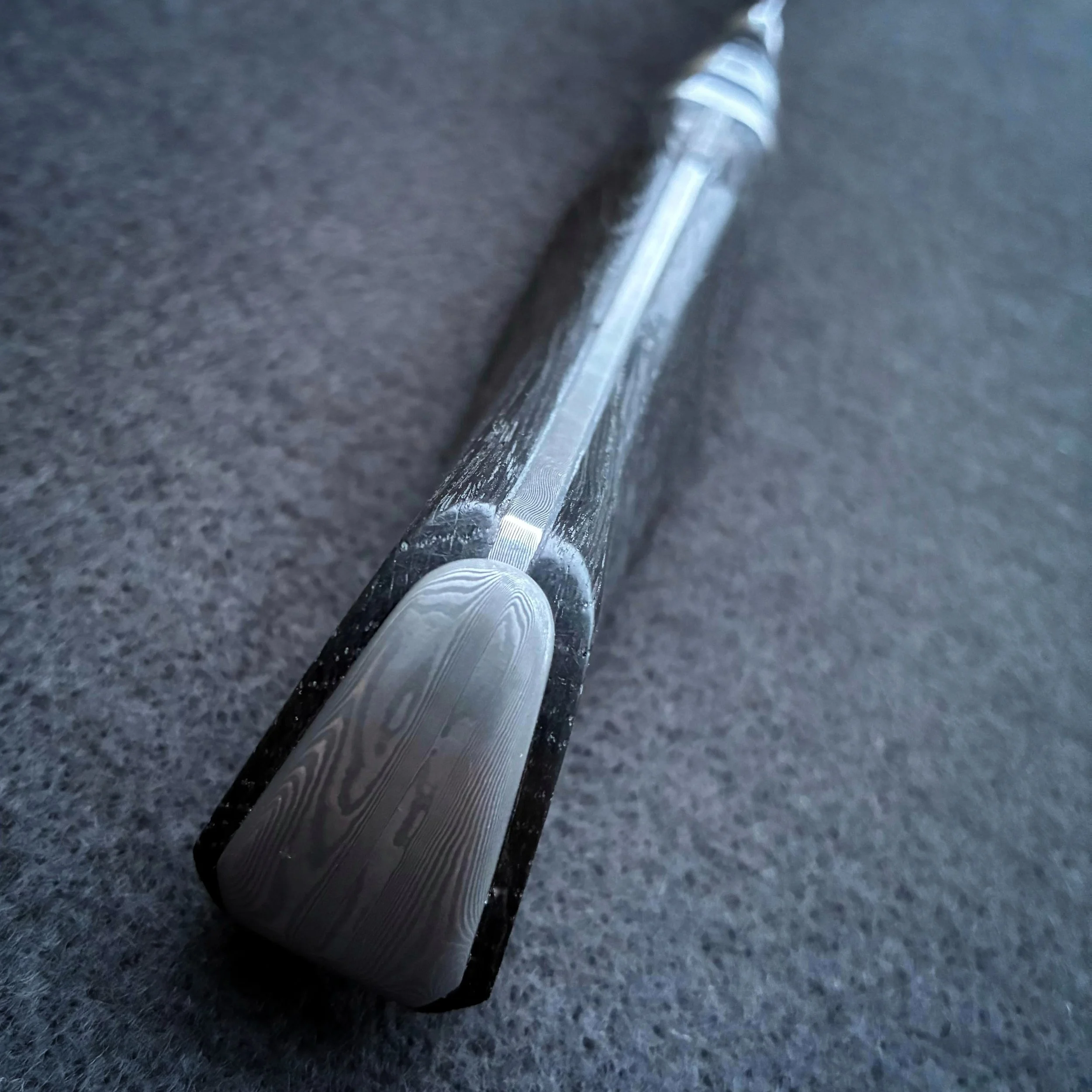 Close-up view of a chef knife handle with a black handle resting on a dark gray surface.