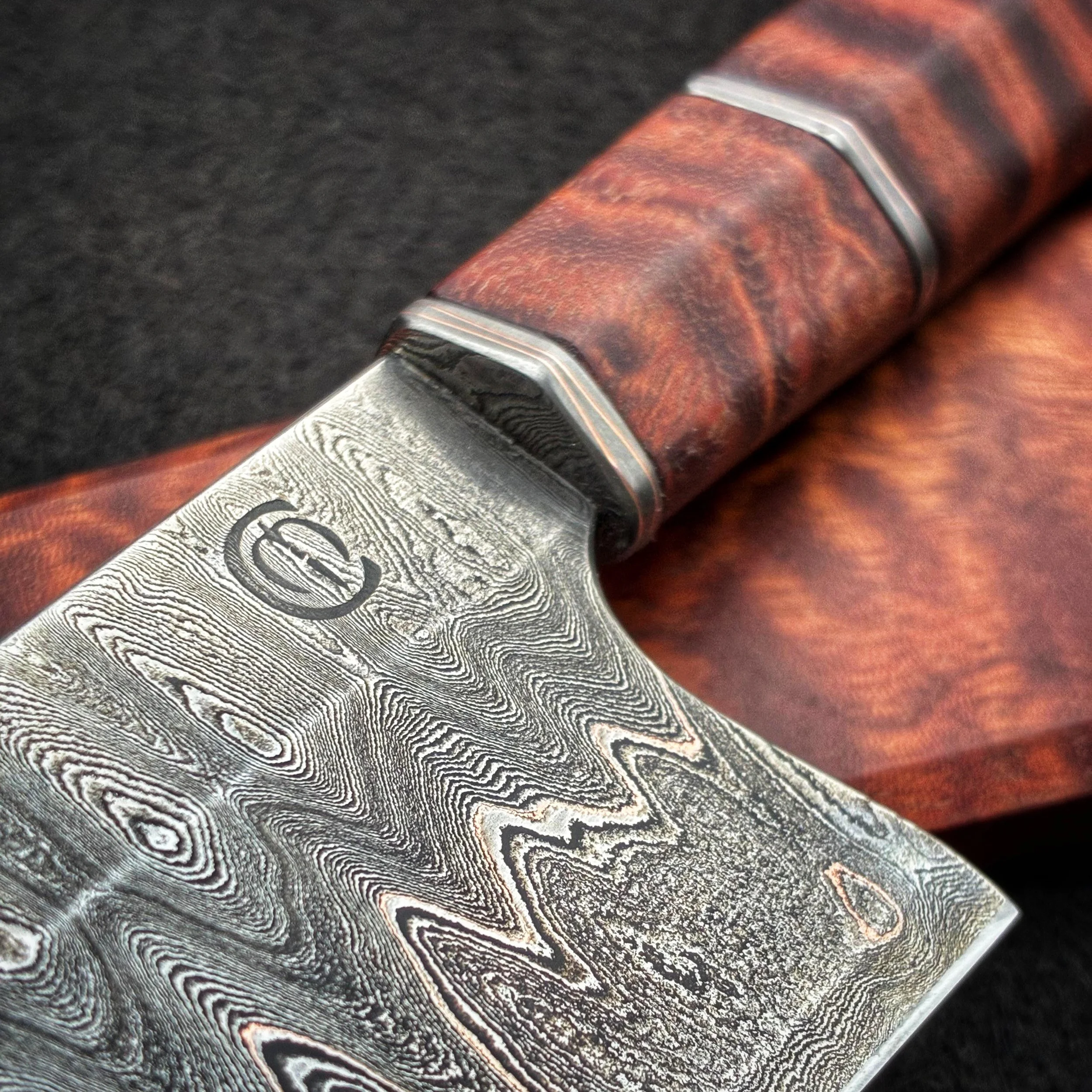 Close-up of a Damascus steel knife with a textured pattern on the blade and a wooden handle against a black background.