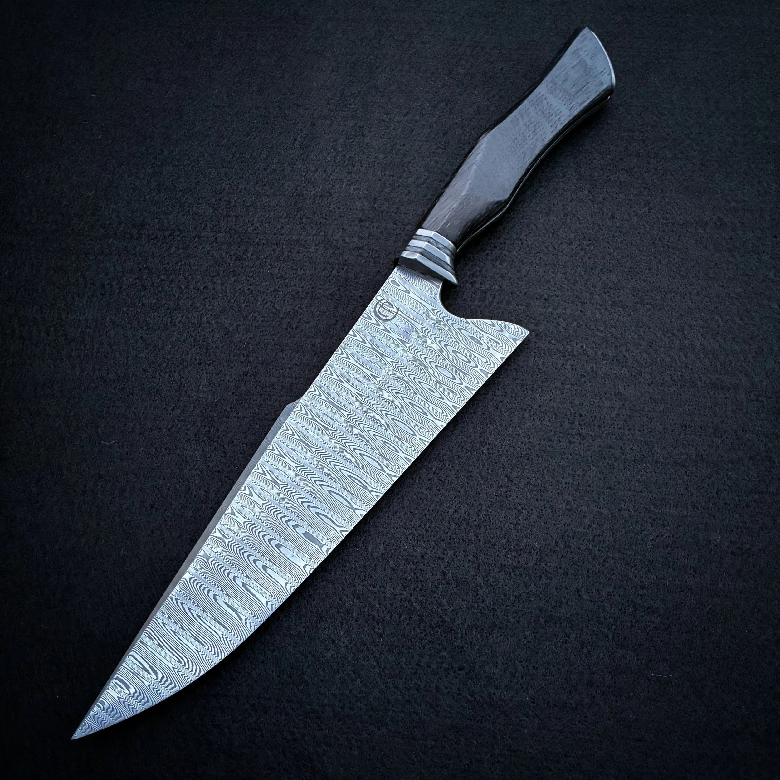 A large chef's kitchen knife with a Damascus steel blade and a dark handle, placed on a black surface.