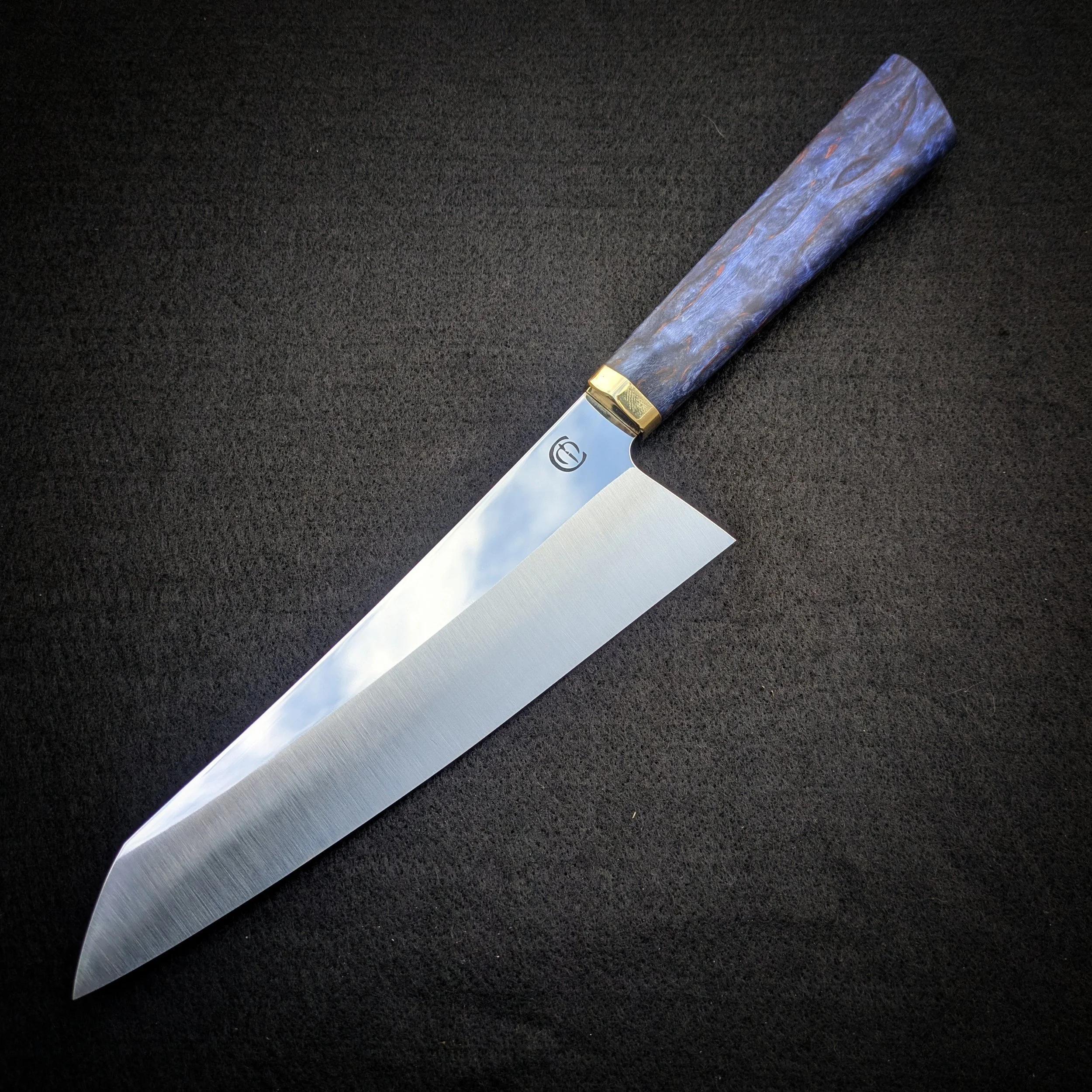 Close-up of a kitchen chef's knife with a patterned handle, resting on a black surface.