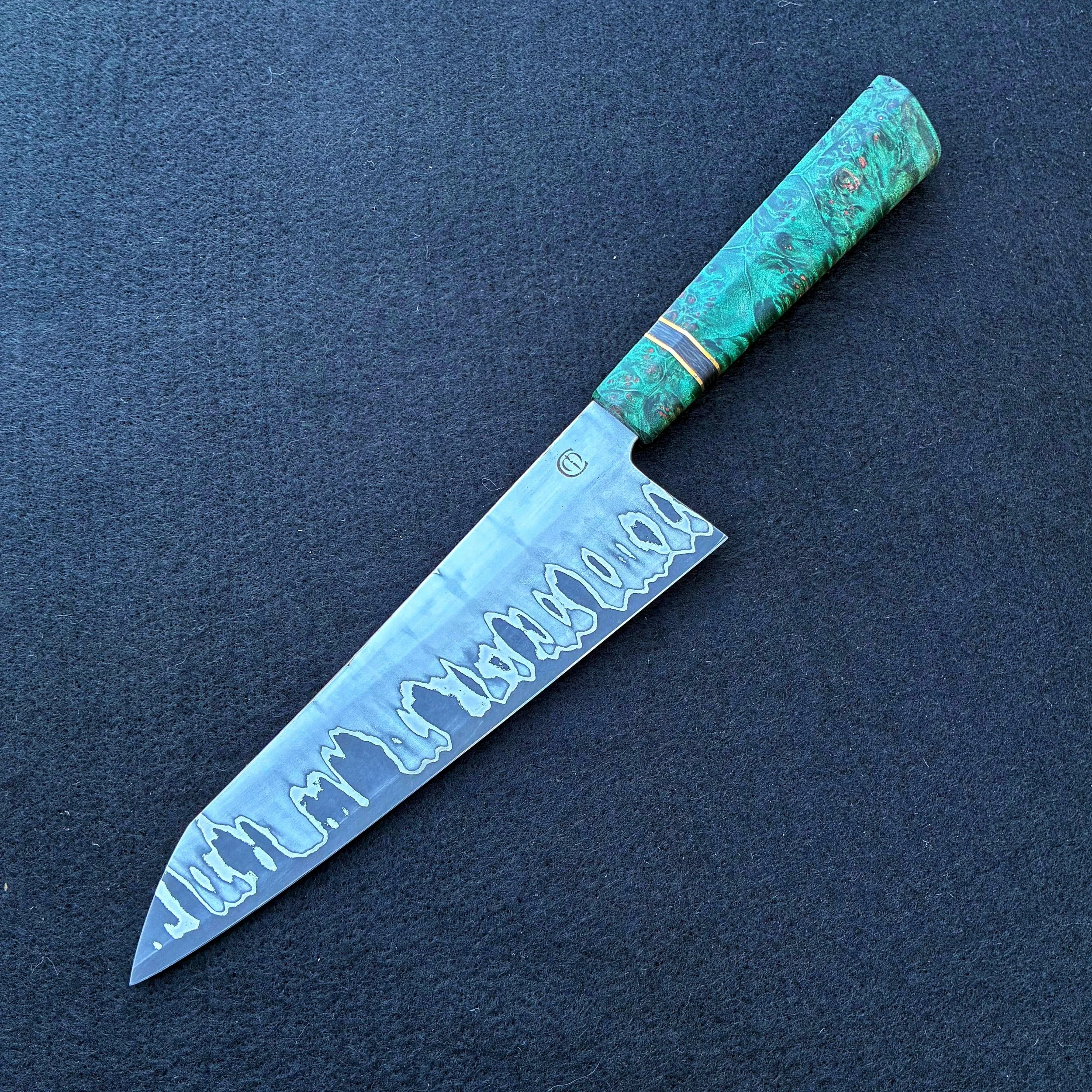 A handcrafted kitchen knife with a patterned green handle and a decorated stainless steel blade against a black background.