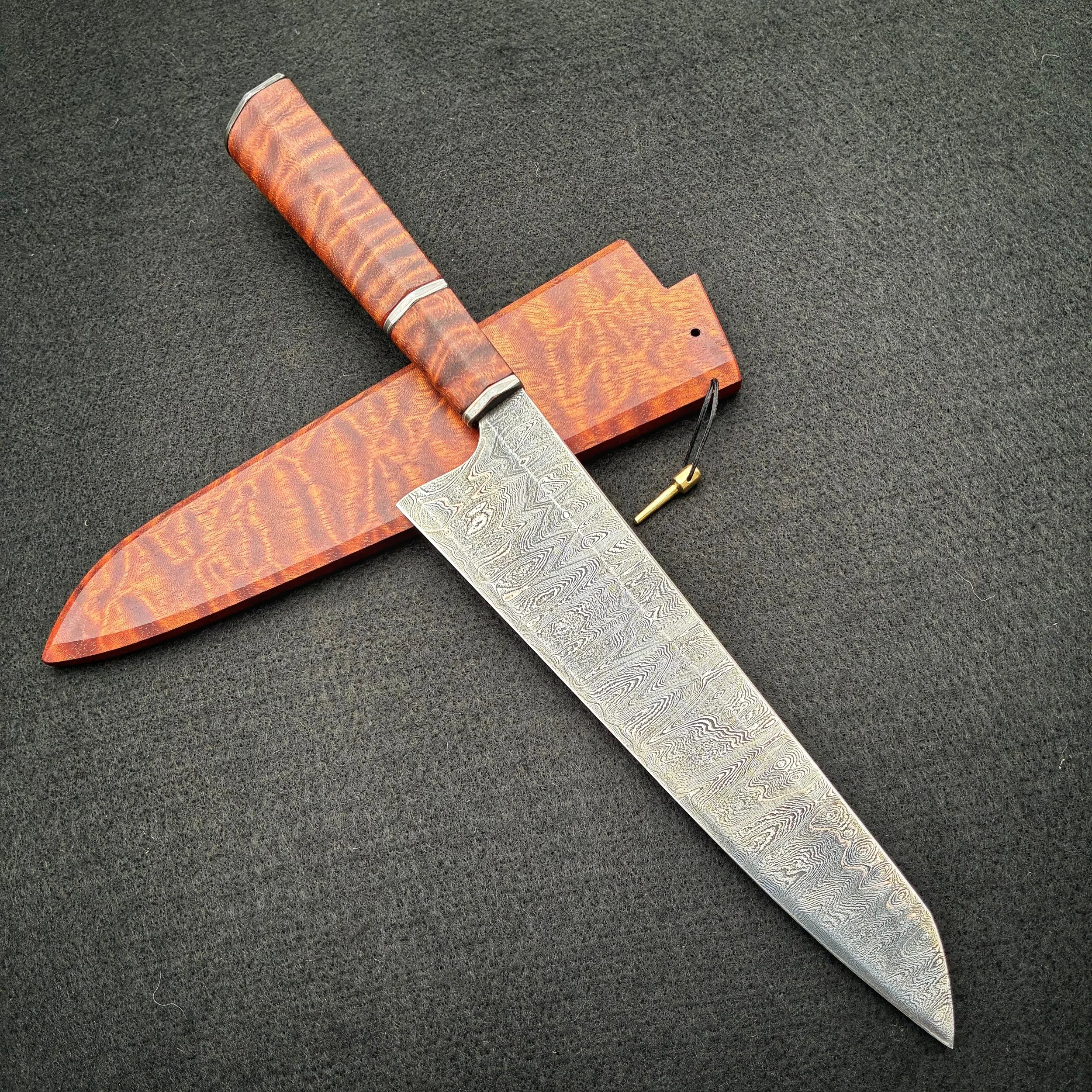 A large knife with a Damascus steel blade, a wood handle, and a wooden sheath on a black surface.