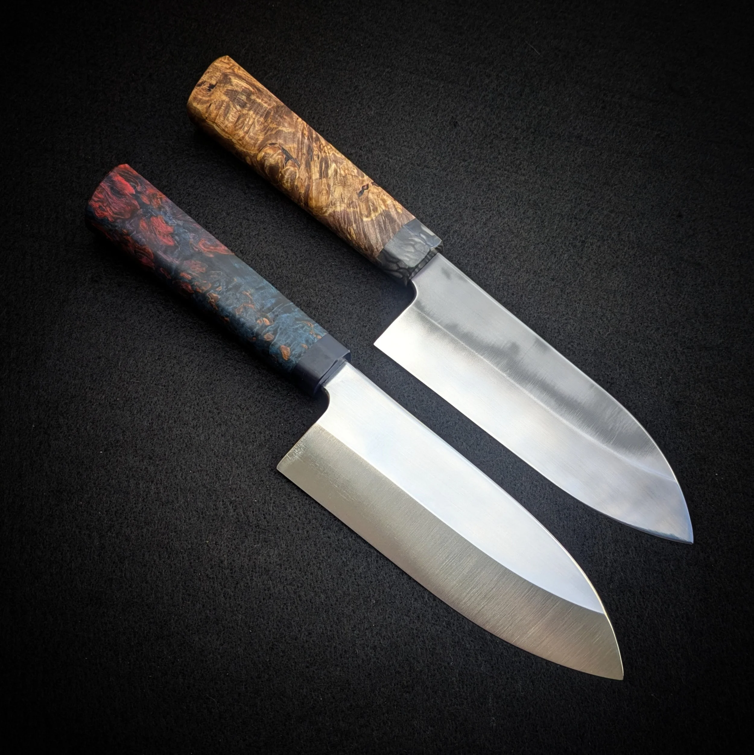 Close-up of two kitchen knives with marbled, multicolored handles on a black surface.