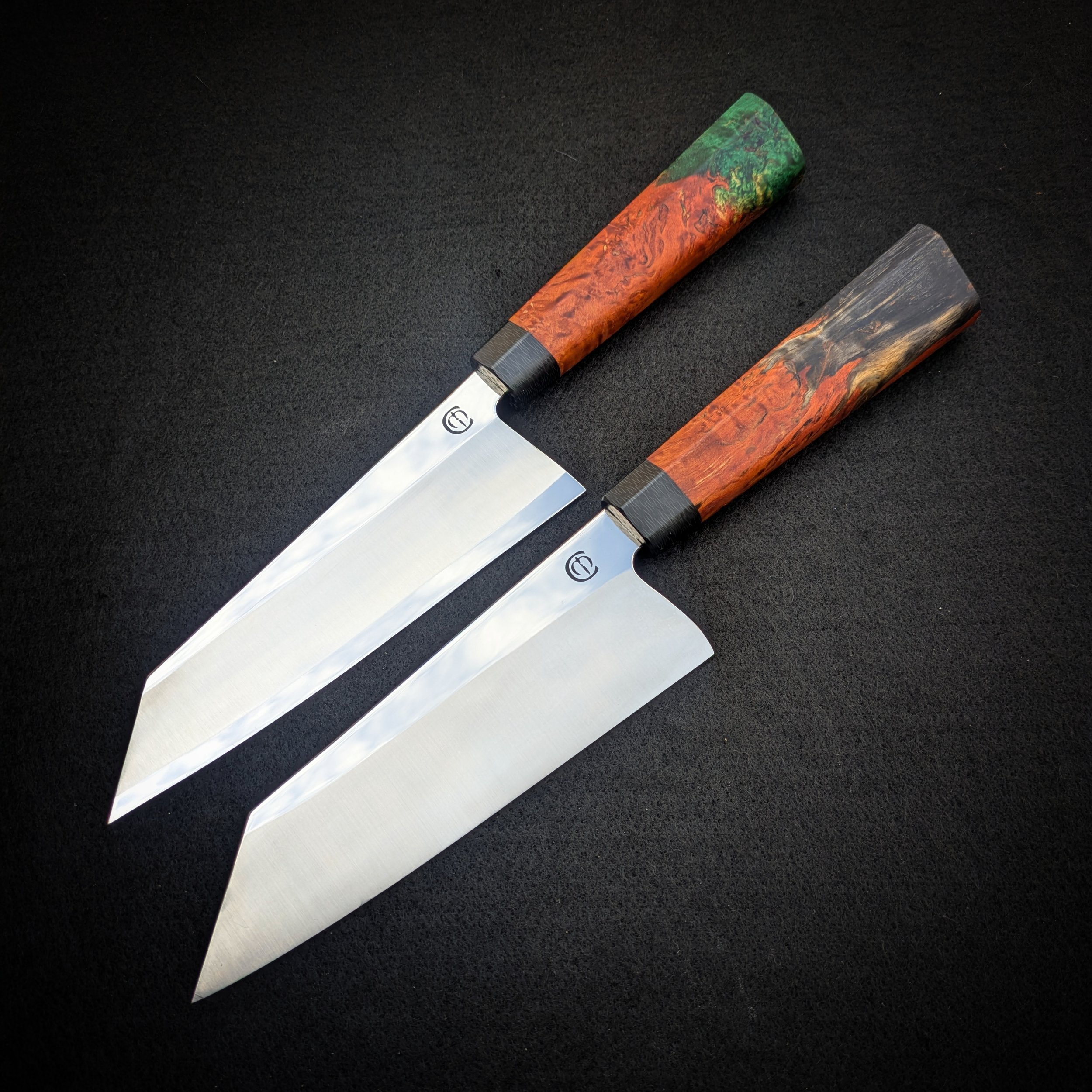 A close-up photo of two knives with colorful handles lying on a black surface. The handles have a wood grain pattern with shades of orange and green.