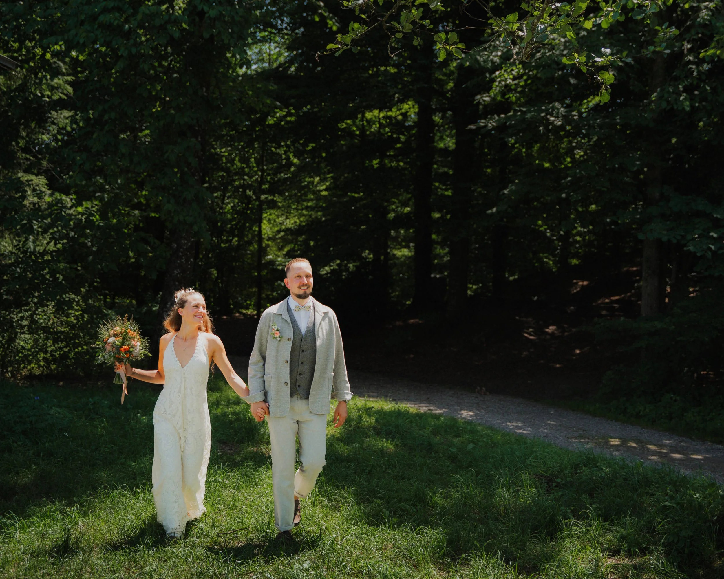 Ein Brautpaar, ein Mann und eine Frau, gehen Hand in Hand durch einen grünen Park, bei einer Hochzeit im Freien.